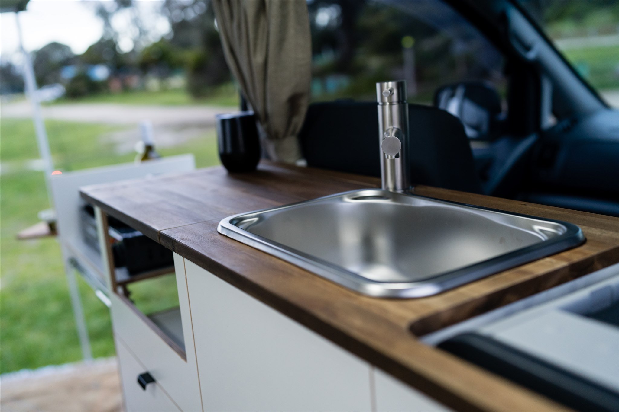 Interior view of a camper van with a small kitchen sink, countertop, and window.