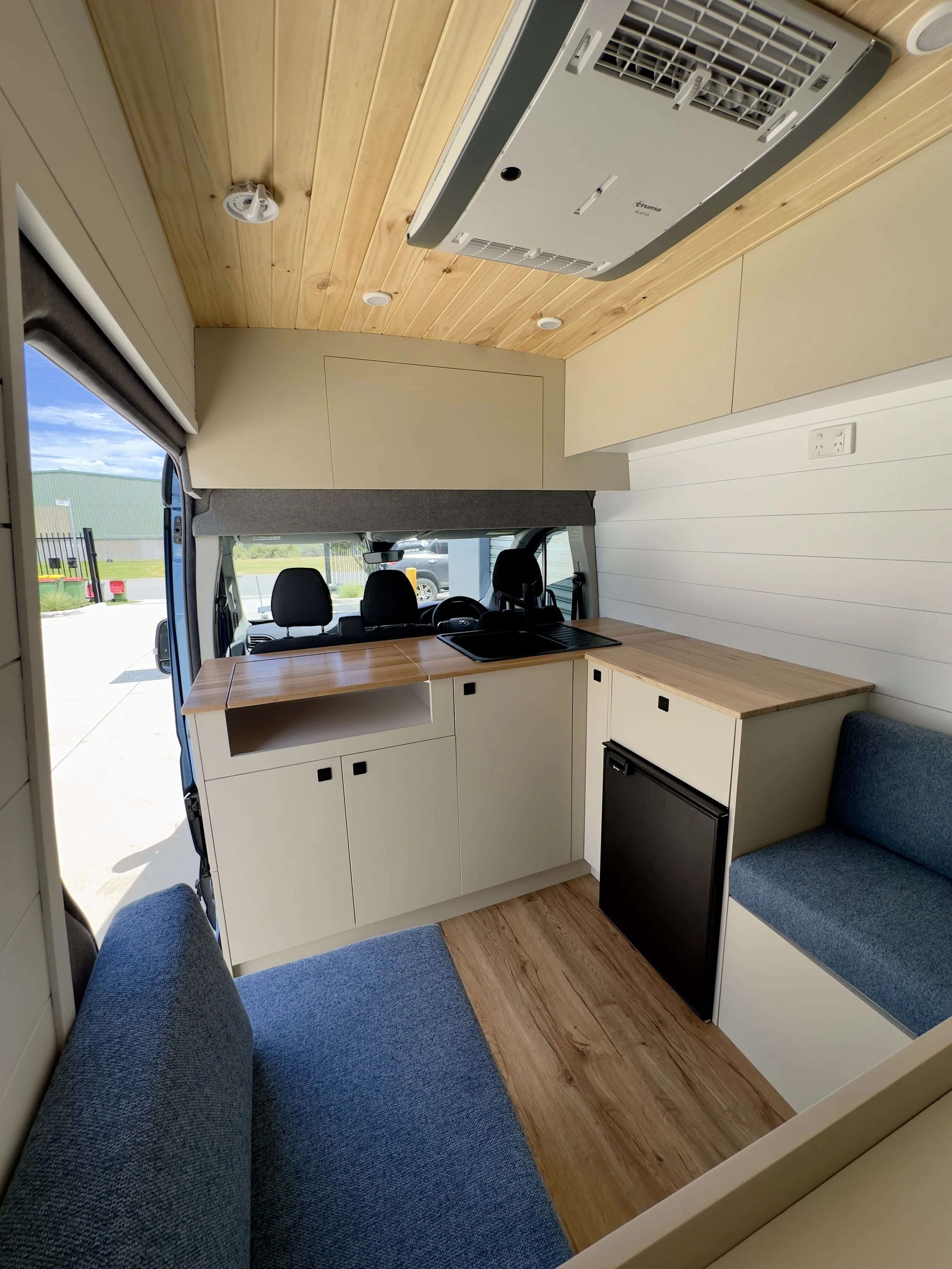 Interior of a tiny home kitchen with wood cabinets, a small refrigerator, sink, and seating area.