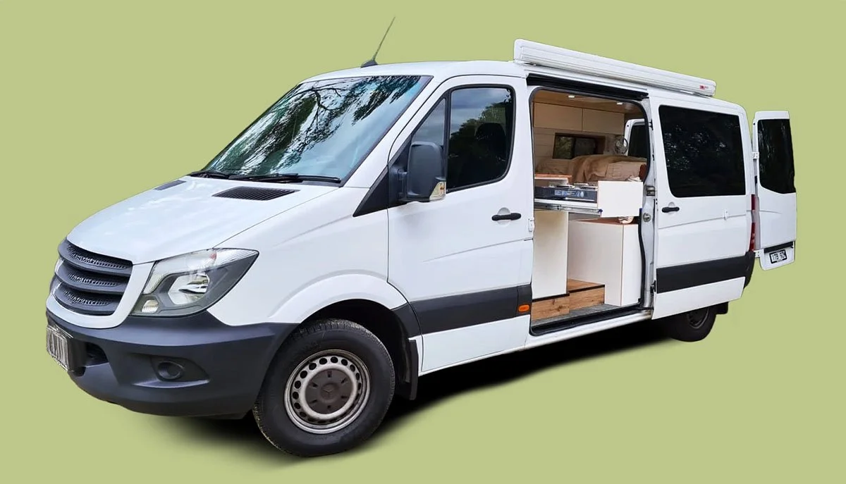 White camper van with sliding door open, showing a small kitchen and interior with a bed.