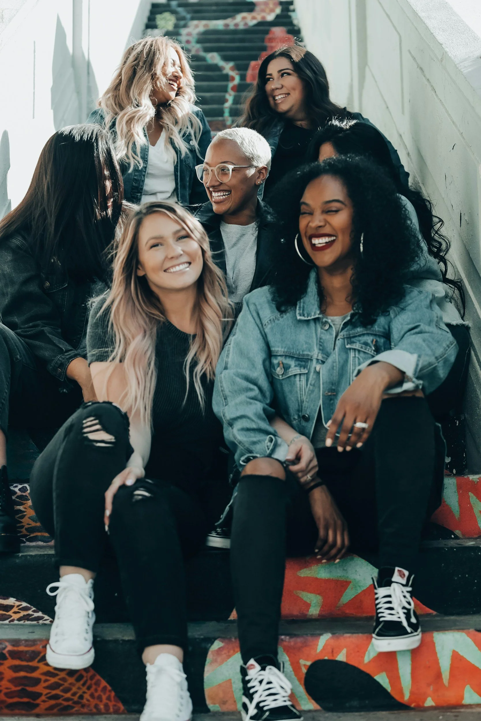 Group of women sitting on colorful stairs, smiling, and enjoying each other's company.