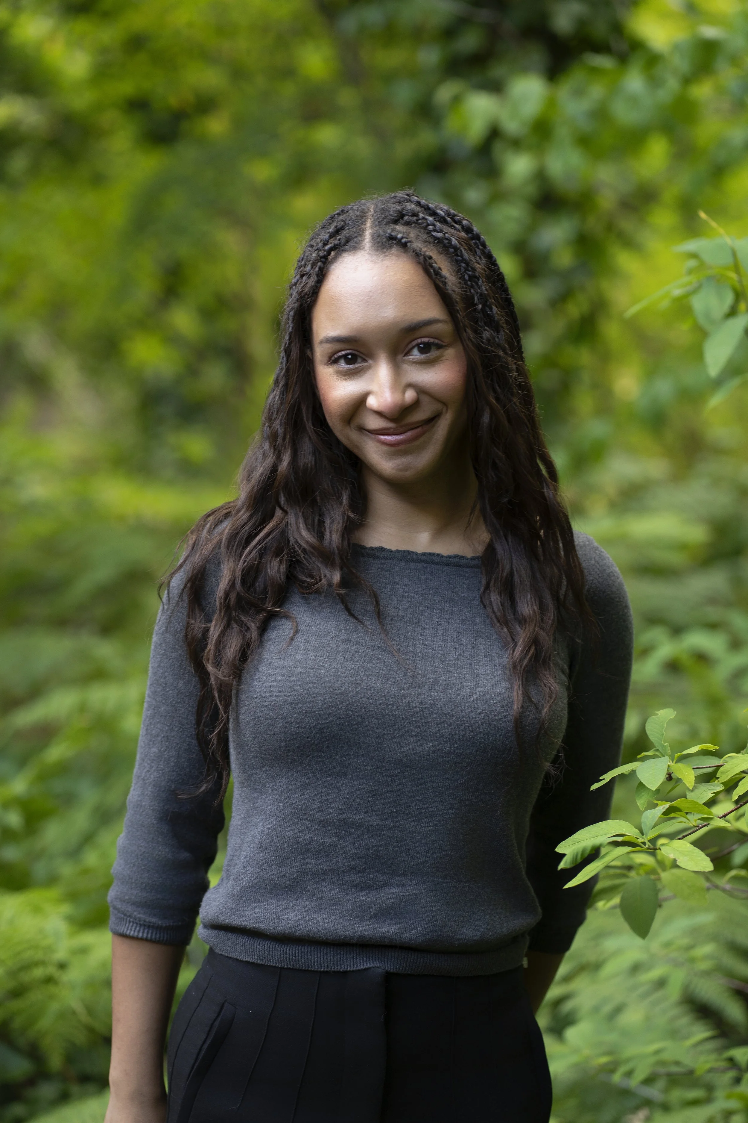 A young woman with dark hair smiling at the camera, wearing a black top, in a neutral background with some flowers.