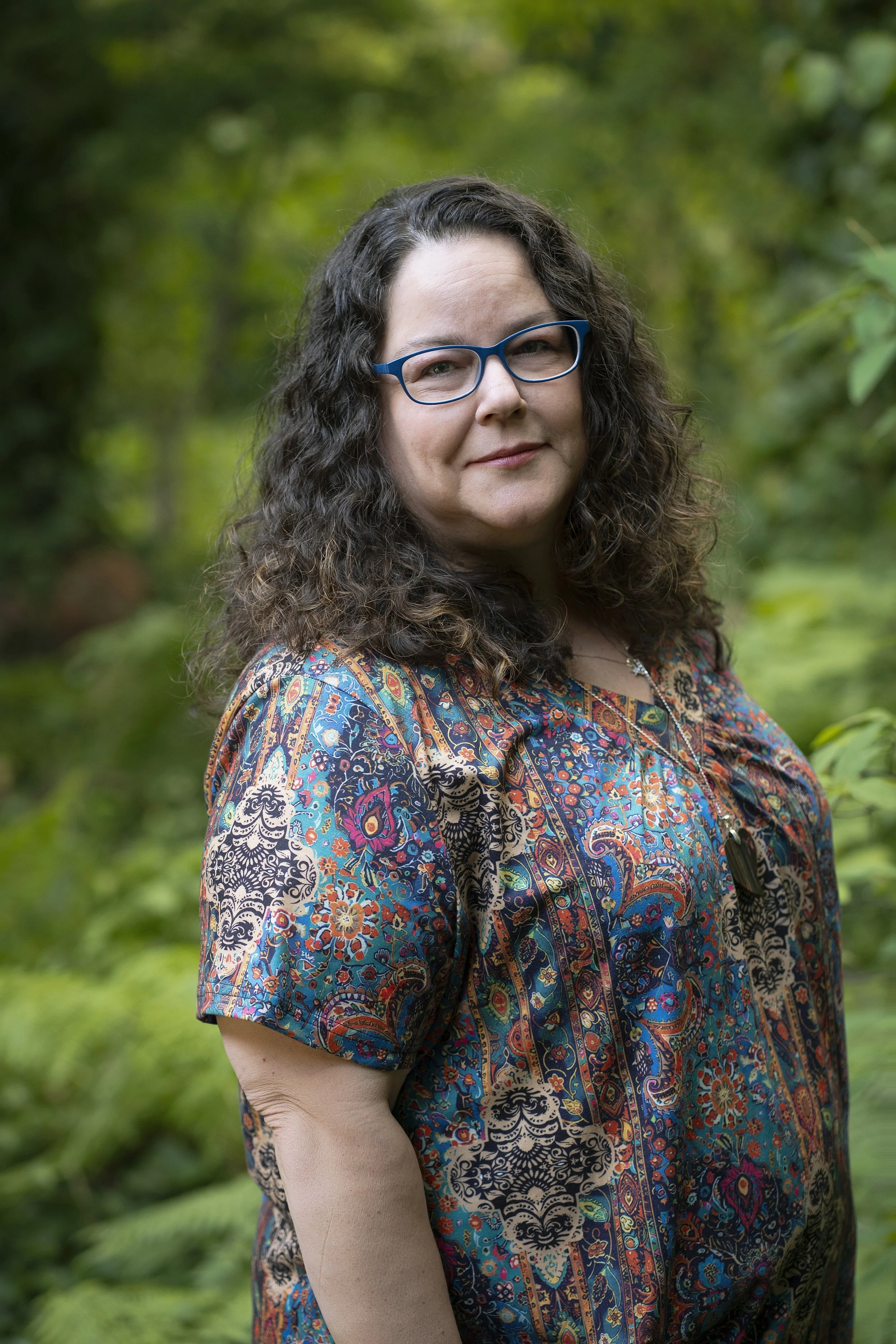 A woman with glasses and long brown hair smiling at the camera.