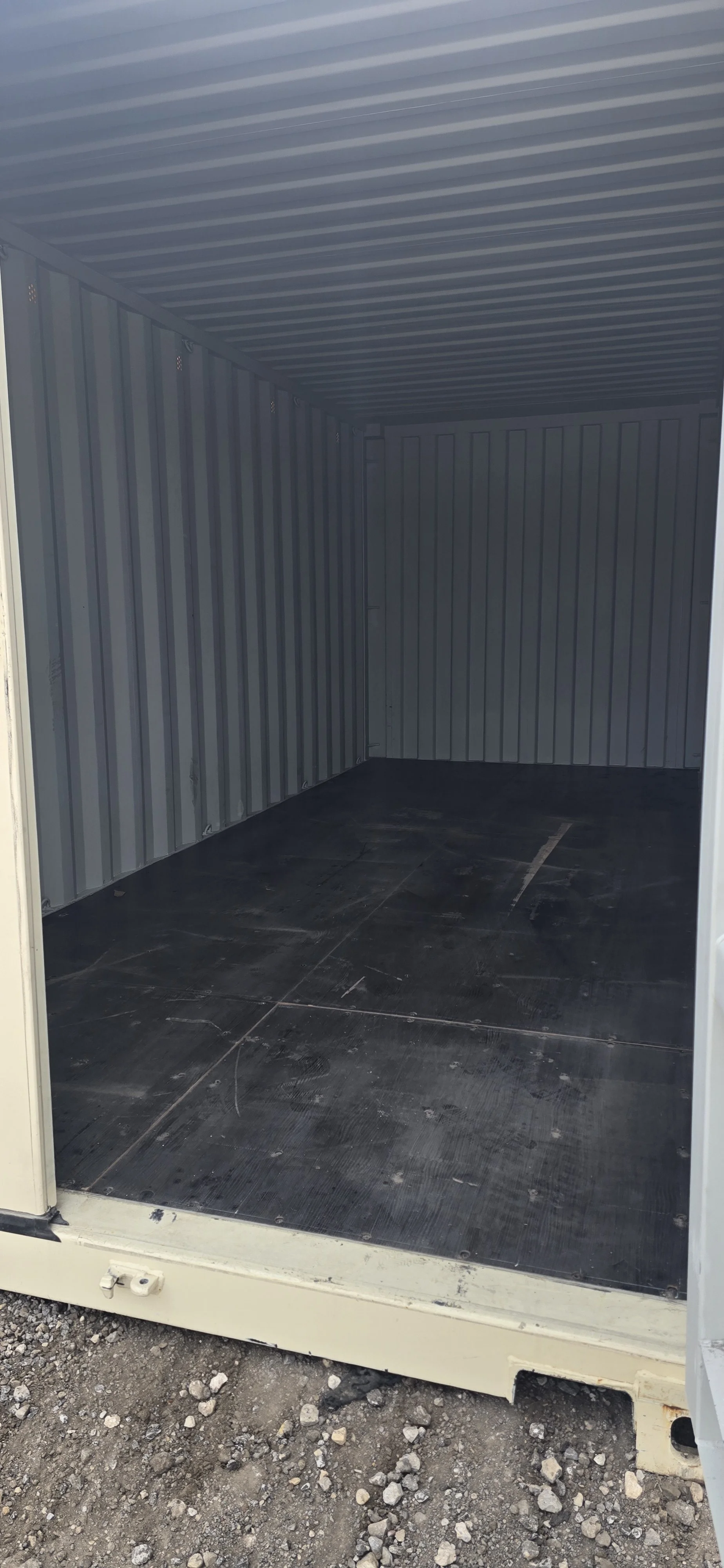Empty storage container with metal walls and floor, situated outdoors on gravel ground.
