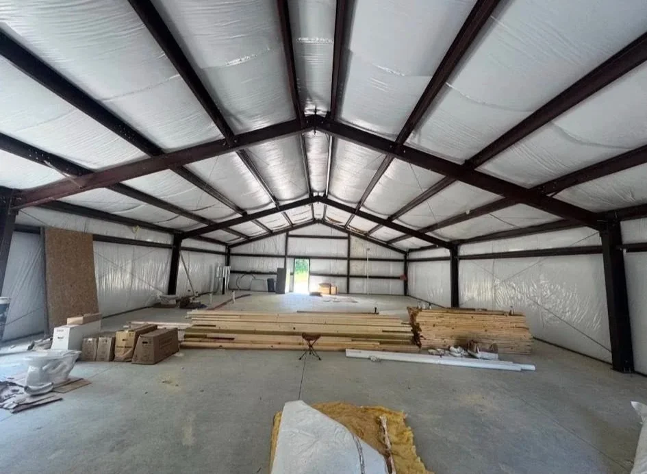 Empty large indoor space under construction with building materials, lumber, and tools scattered around.