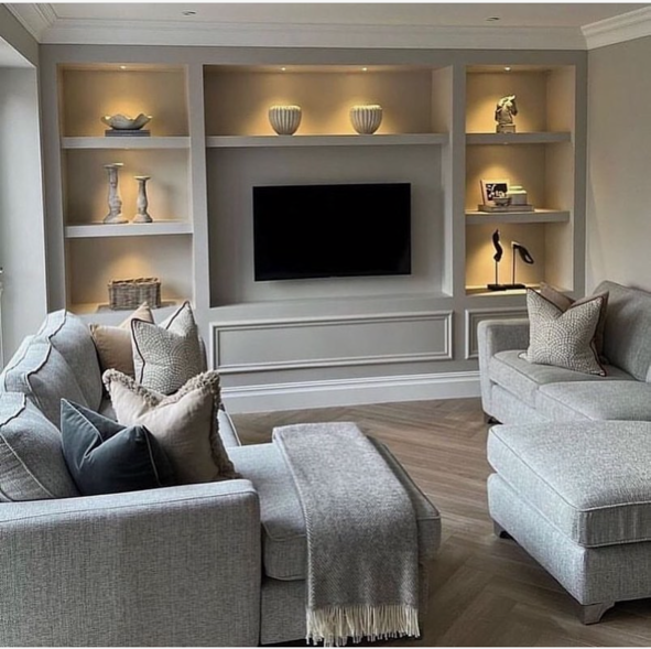 Living room with built-in shelves, a wall-mounted TV, and light gray sofas with pillows.