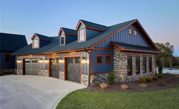 Modern blue house with stone accents, three garage doors, dormer windows, and landscaped yard.