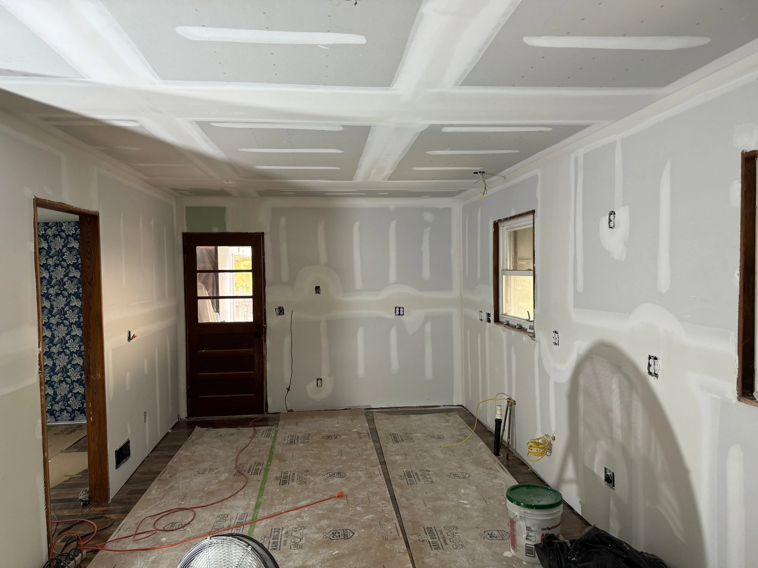 Interior of a room under construction with drywall, exposed electrical wiring, and windows.