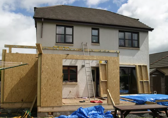 Under construction residential building with wooden framing, a ladder, and blue tarps on the ground.