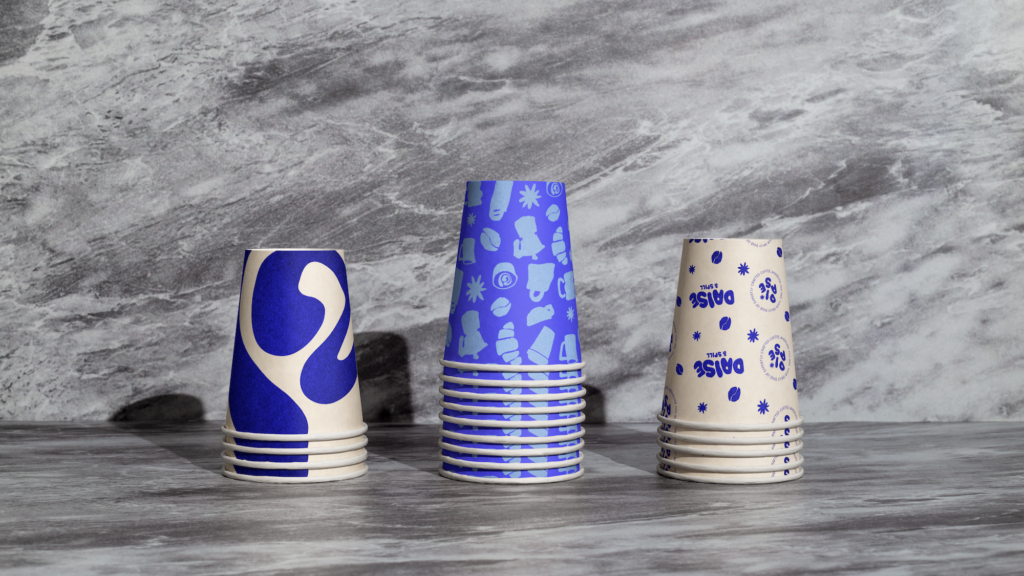 Stack of paper coffee cups with blue and white designs on a wooden surface, with a gray textured background.