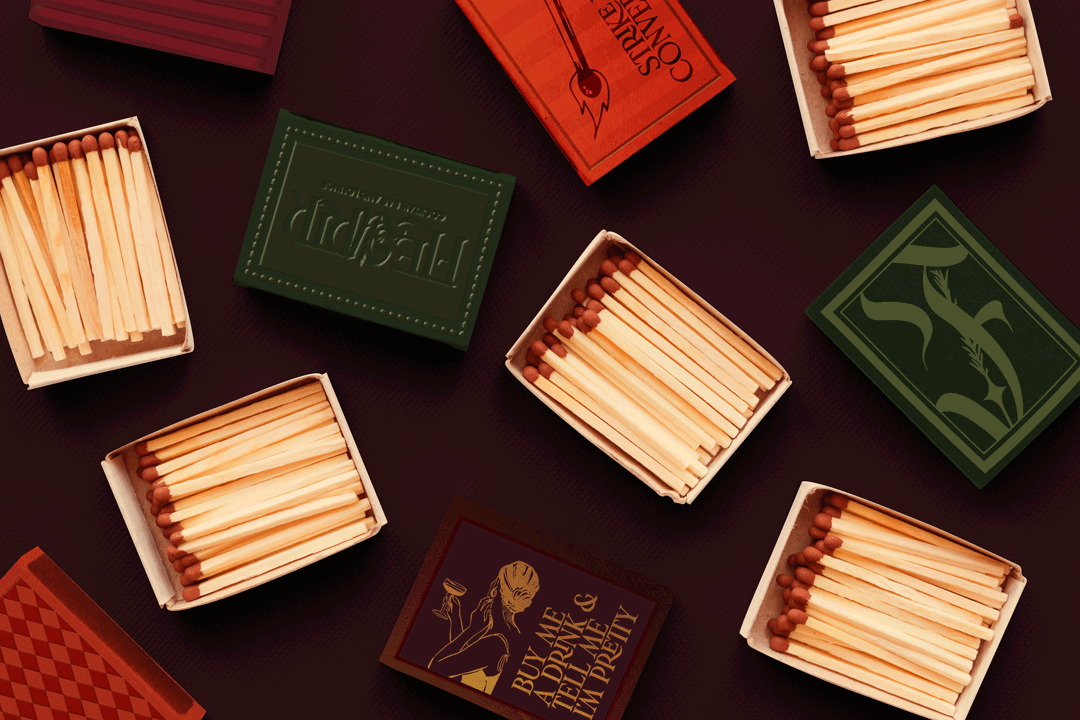 Multiple open matchboxes with wooden matches on a dark surface, colorful matchbox covers with various designs and text.