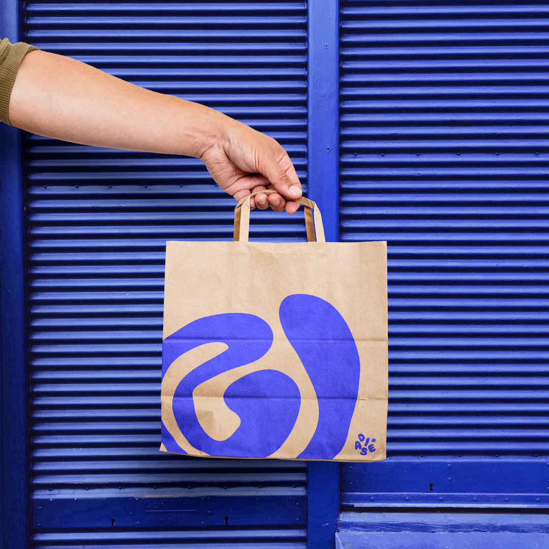 A hand holding a paper shopping bag with blue abstract design against a blue textured background.