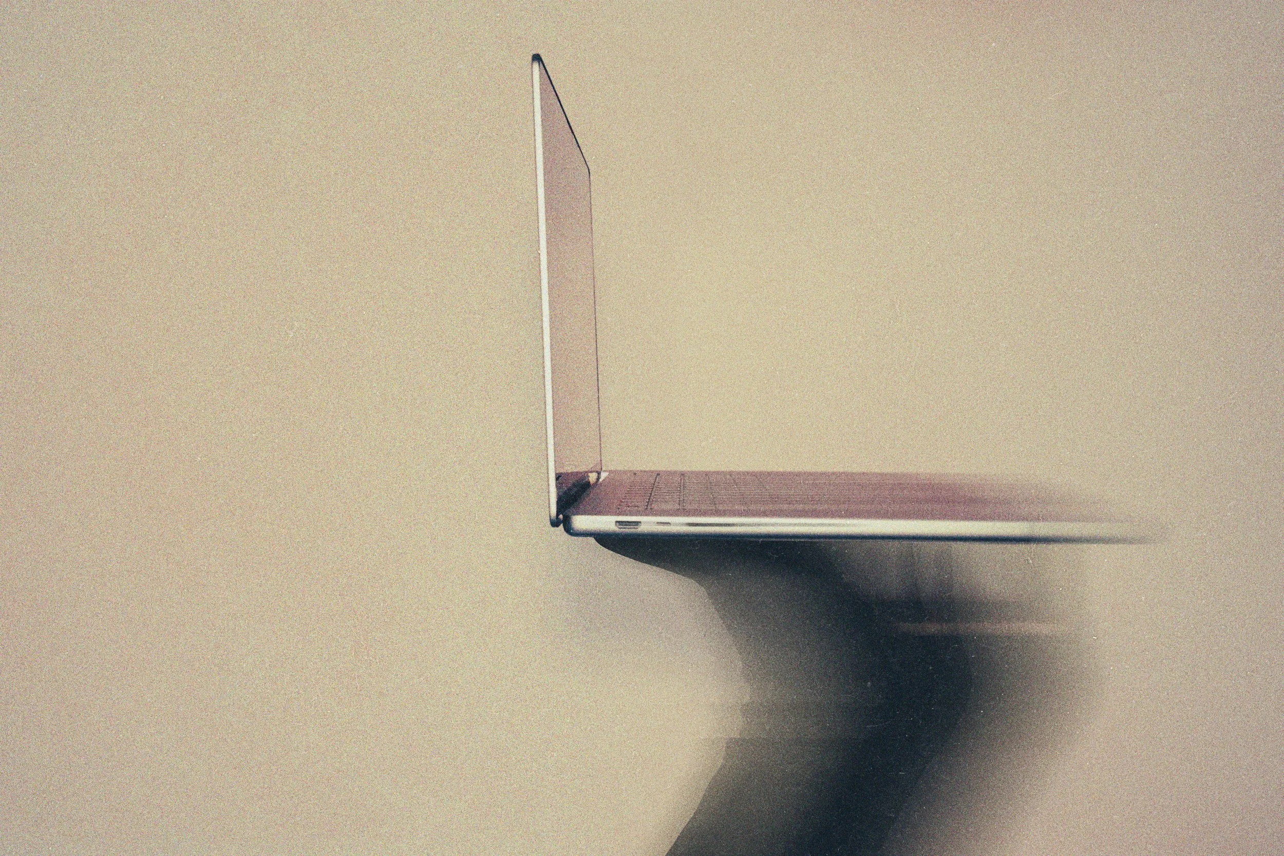 Side view of an open laptop with a blank screen, positioned on a dark surface against a beige background.