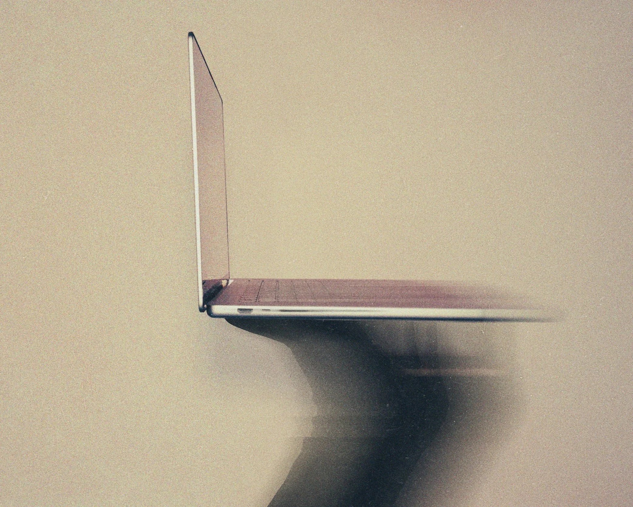 Silver laptop opened on a beige wall, with a person's hand holding it from underneath.