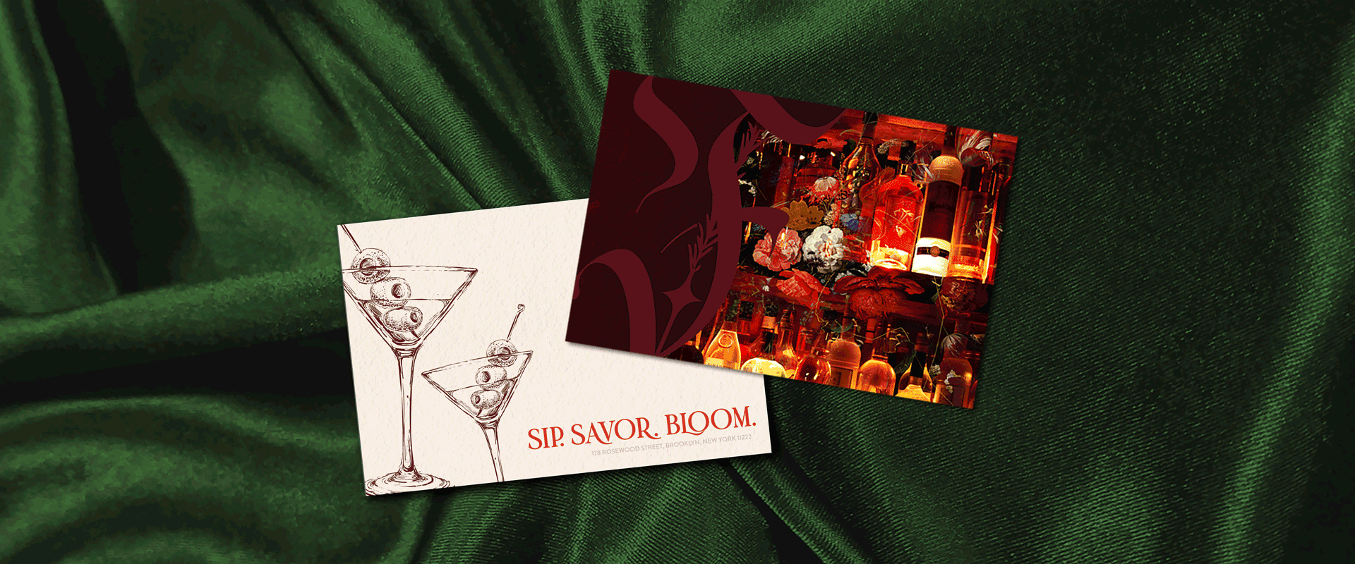 A white card with illustrations of martini glasses and the text "SIP. SAVOR. BLOOM." on green velvet fabric, alongside a colorful, illuminated magazine or photograph of bottles and flowers.
