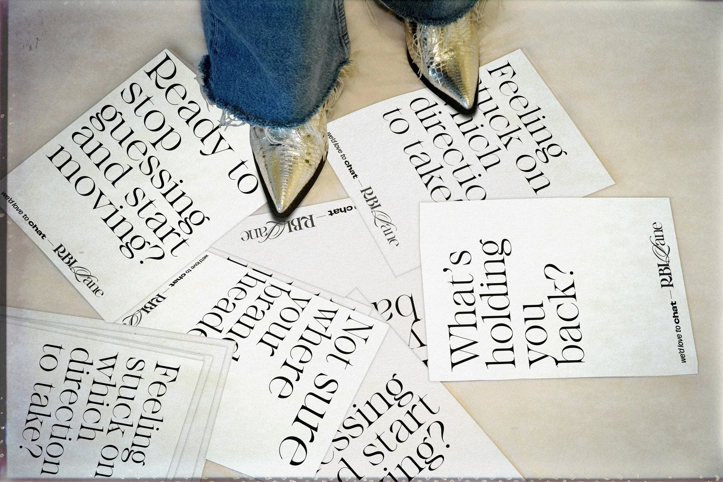 Several printed sheets of paper with questions about love and relationships scattered on a table, with a person wearing shiny boots and jeans standing over them.