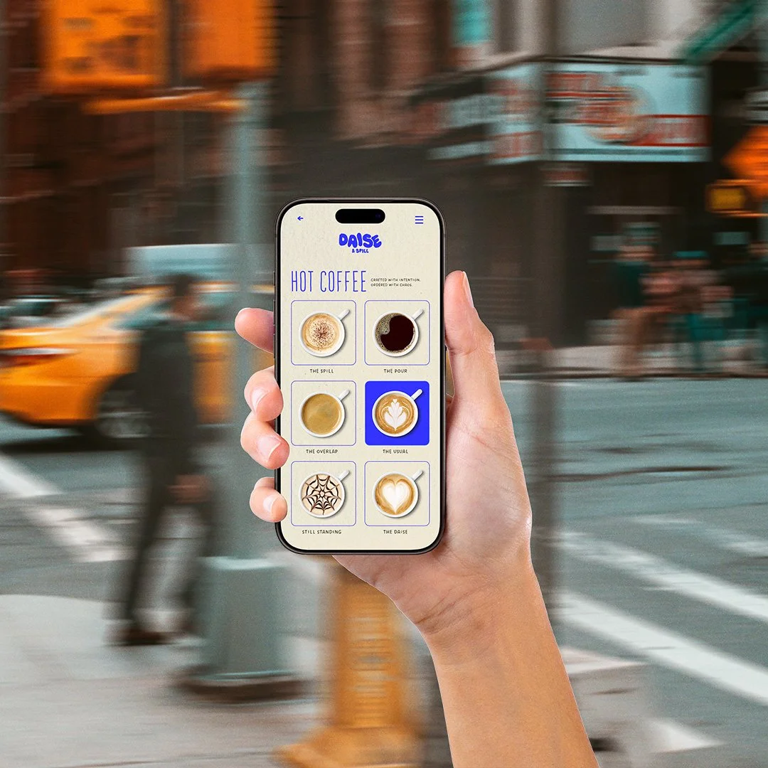 Person holding a smartphone with a coffee ordering app open, showing different coffee drink options on a busy city street background.