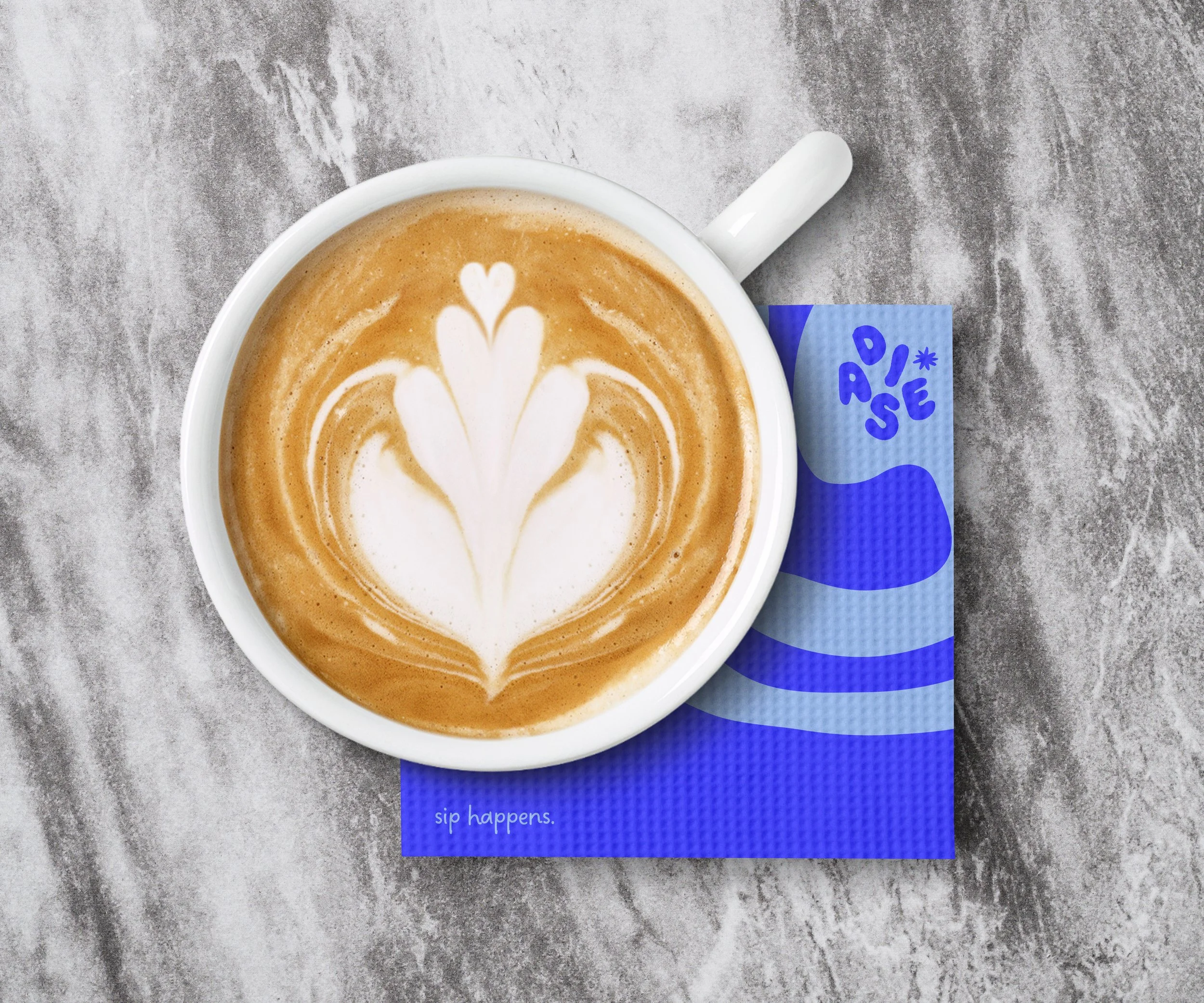 A cup of latte with heart-shaped latte art on top, resting on a blue napkin with the words "sip happens" printed on it, on a gray textured surface.