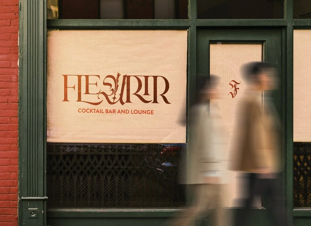 Blurred image of two people walking past a window with a sign that reads 'Fleurir Cocktail Bar and Lounge'.