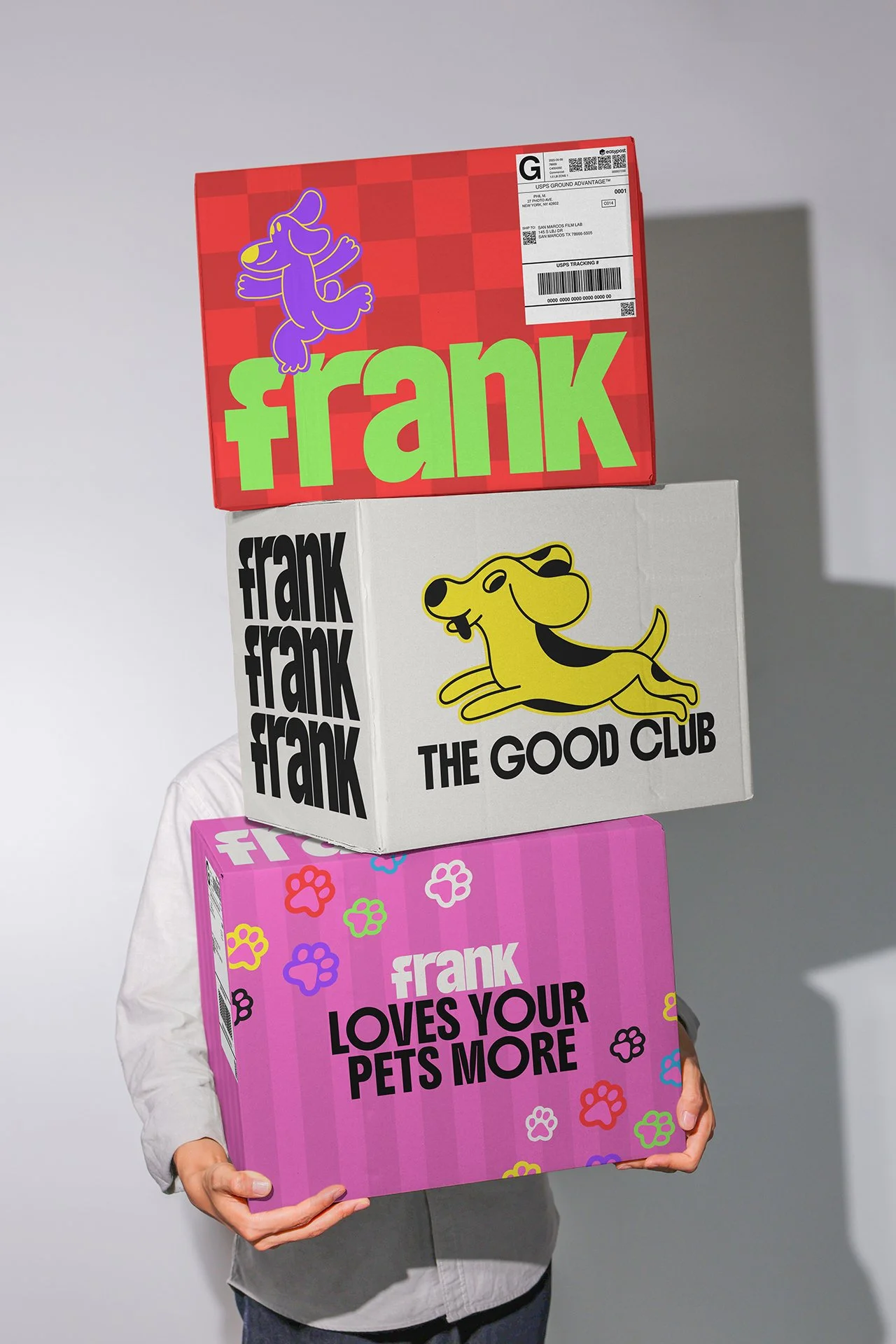 Person holding three colorful boxes with 'Frank' branding, featuring various playful designs and slogans.