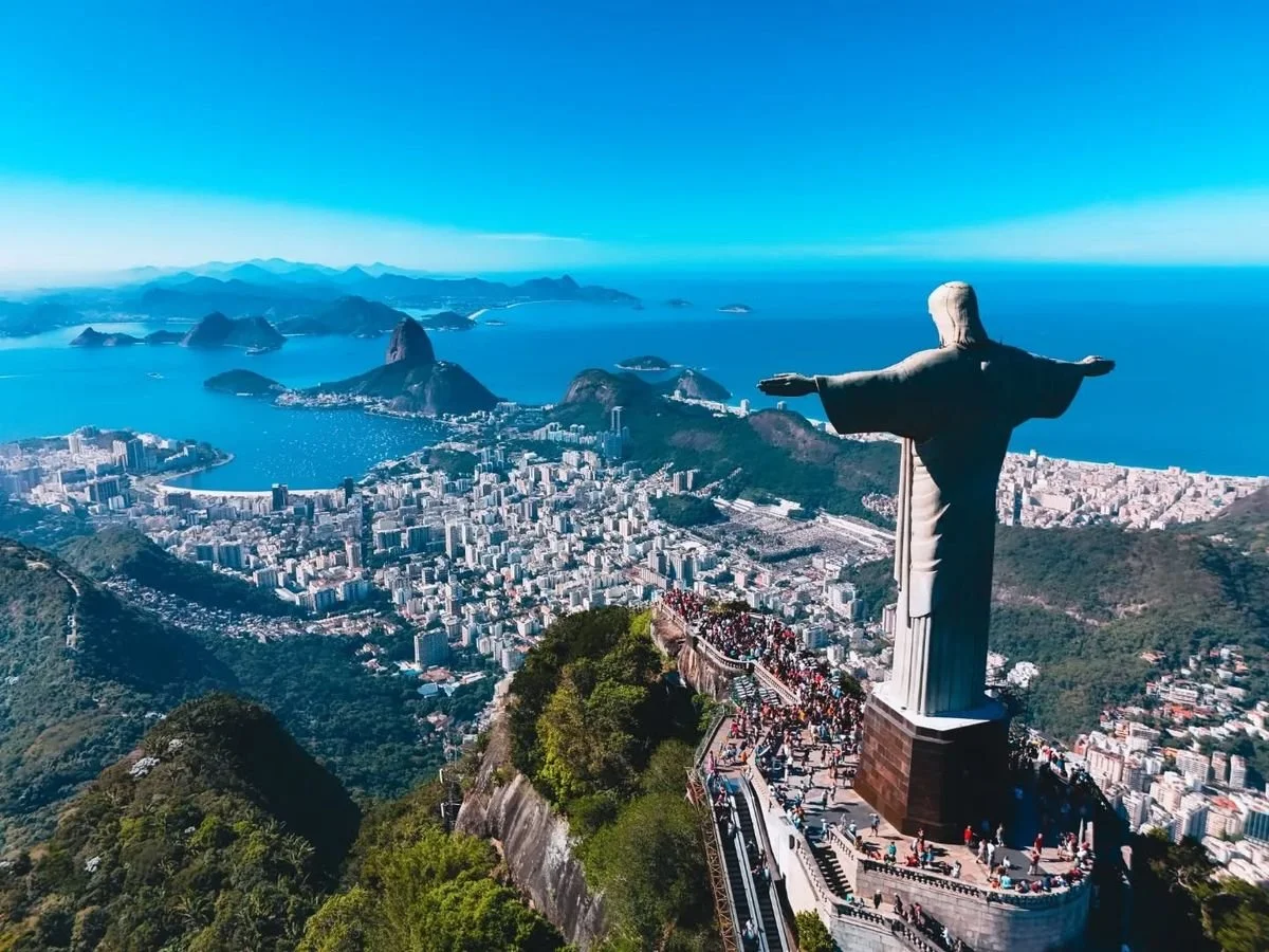 View of Rio de Janeiro from Corcovado with Christ the Redeemer statue in the foreground, overlooking the city, mountains, and ocean on a clear day.