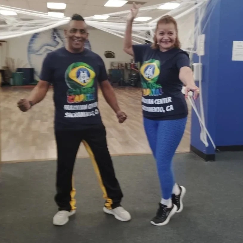 Two smiling people wearing matching t-shirts, standing inside a room decorated with fake spider webs, celebrating or participating in an event.