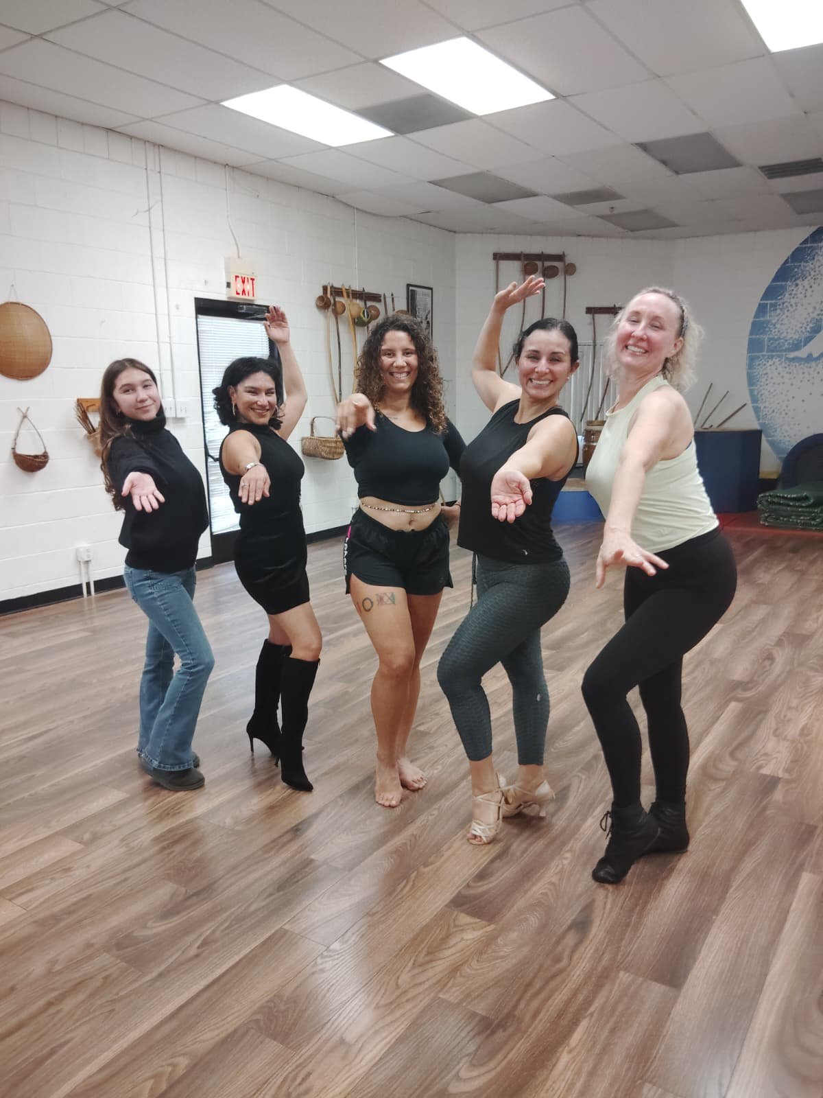 Five women dancing together in a dance studio, posing with lively expressions and arm gestures.