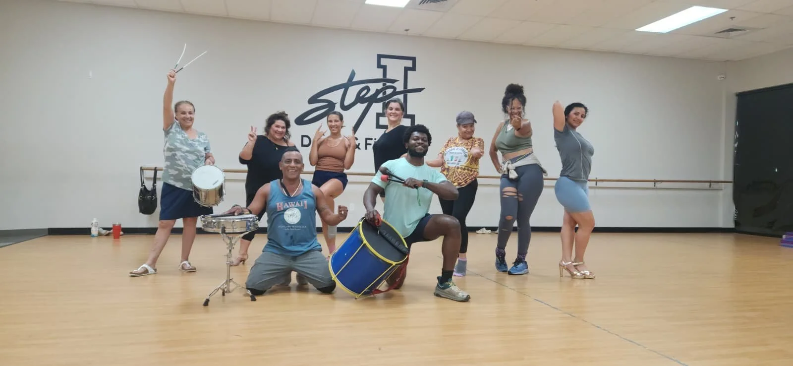 Group of nine diverse people in a dance studio, holding musical instruments and striking playful poses, with a large 'Stop' sign on the wall behind them. sacramento brazilian dance samba class