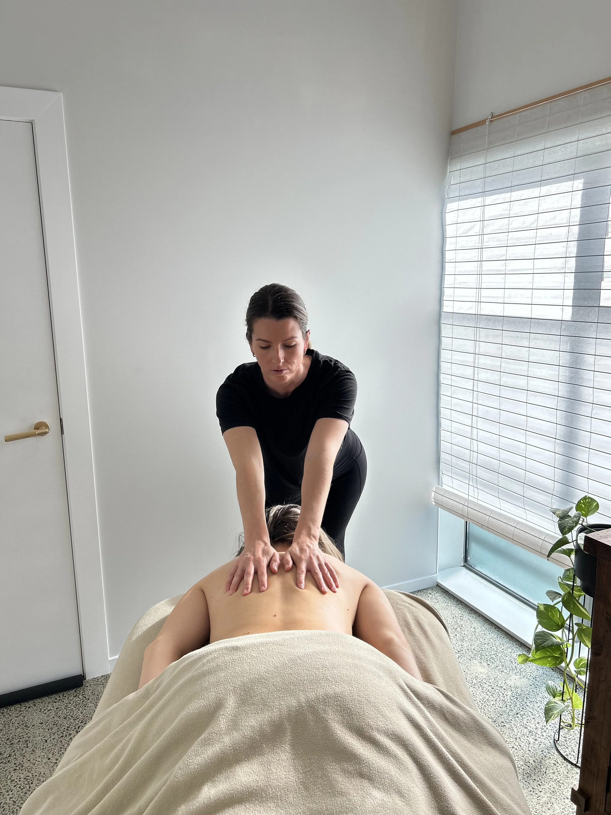 A masseuse giving a back massage to a person lying face down on a massage table.