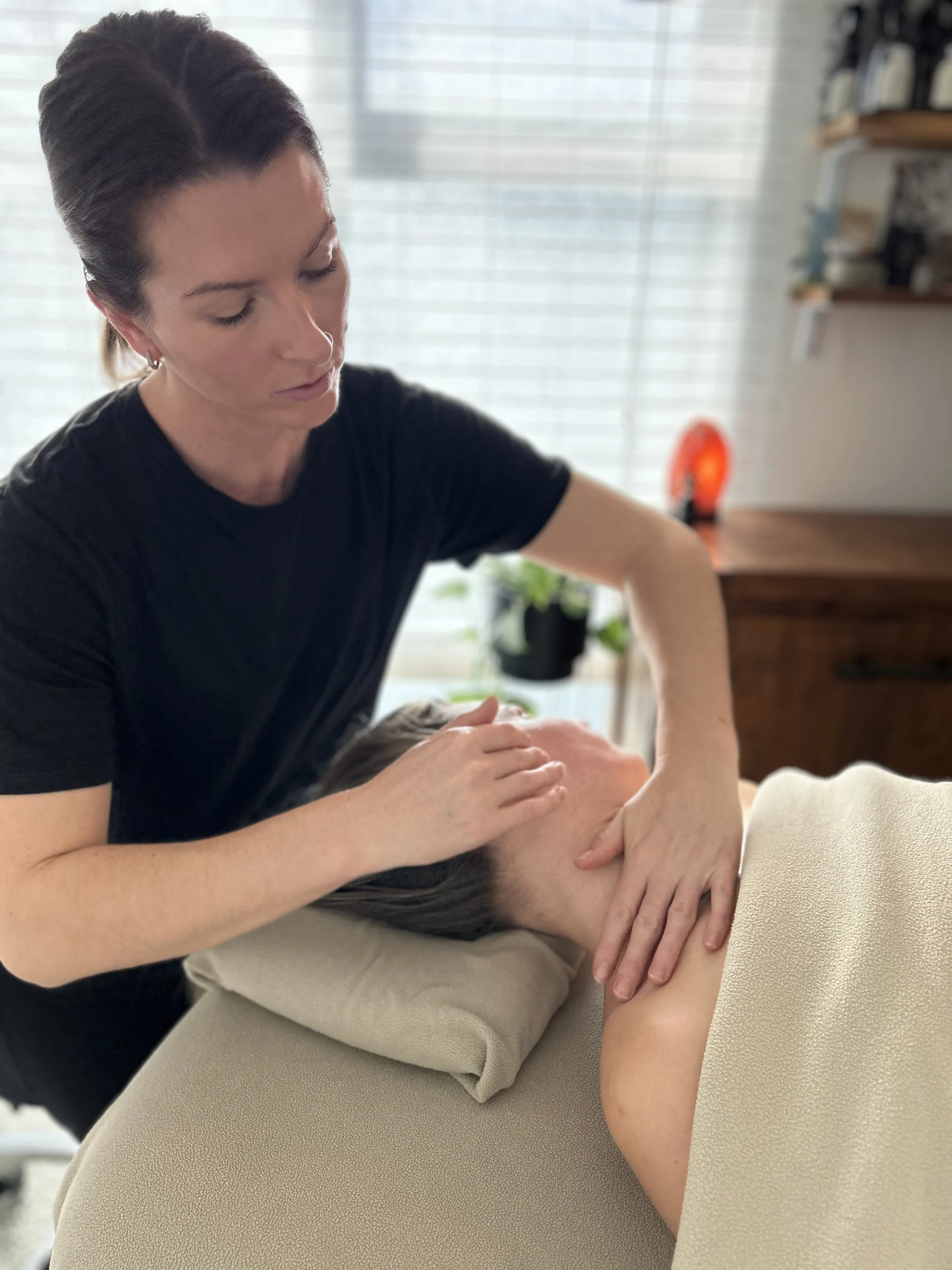 A woman giving a massage to another person lying face up on a massage table.