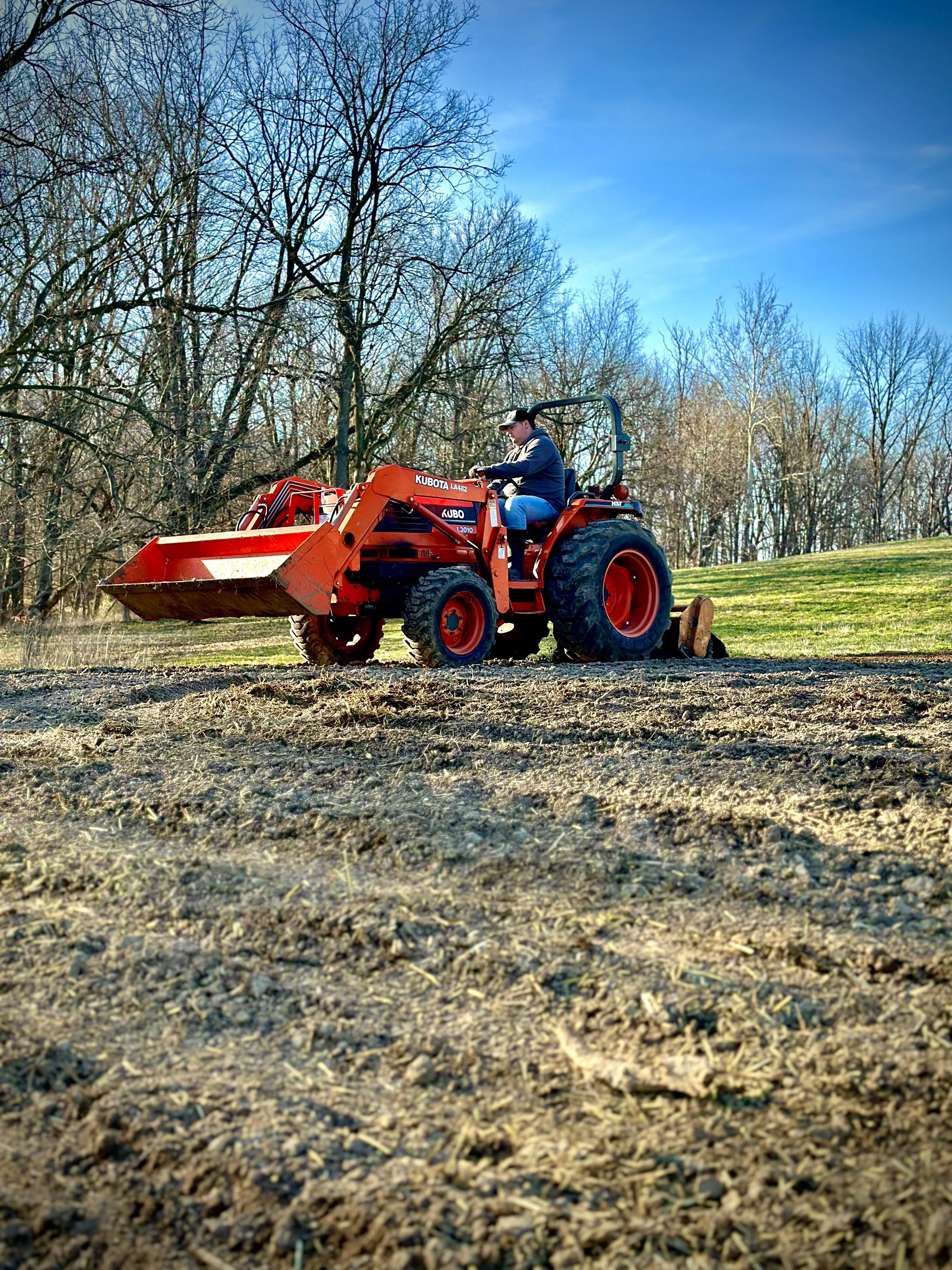 Codie Brewer operating an orange tractor on the Brewer family homestead, preparing the garden for the Farmstand in rural Indiana.