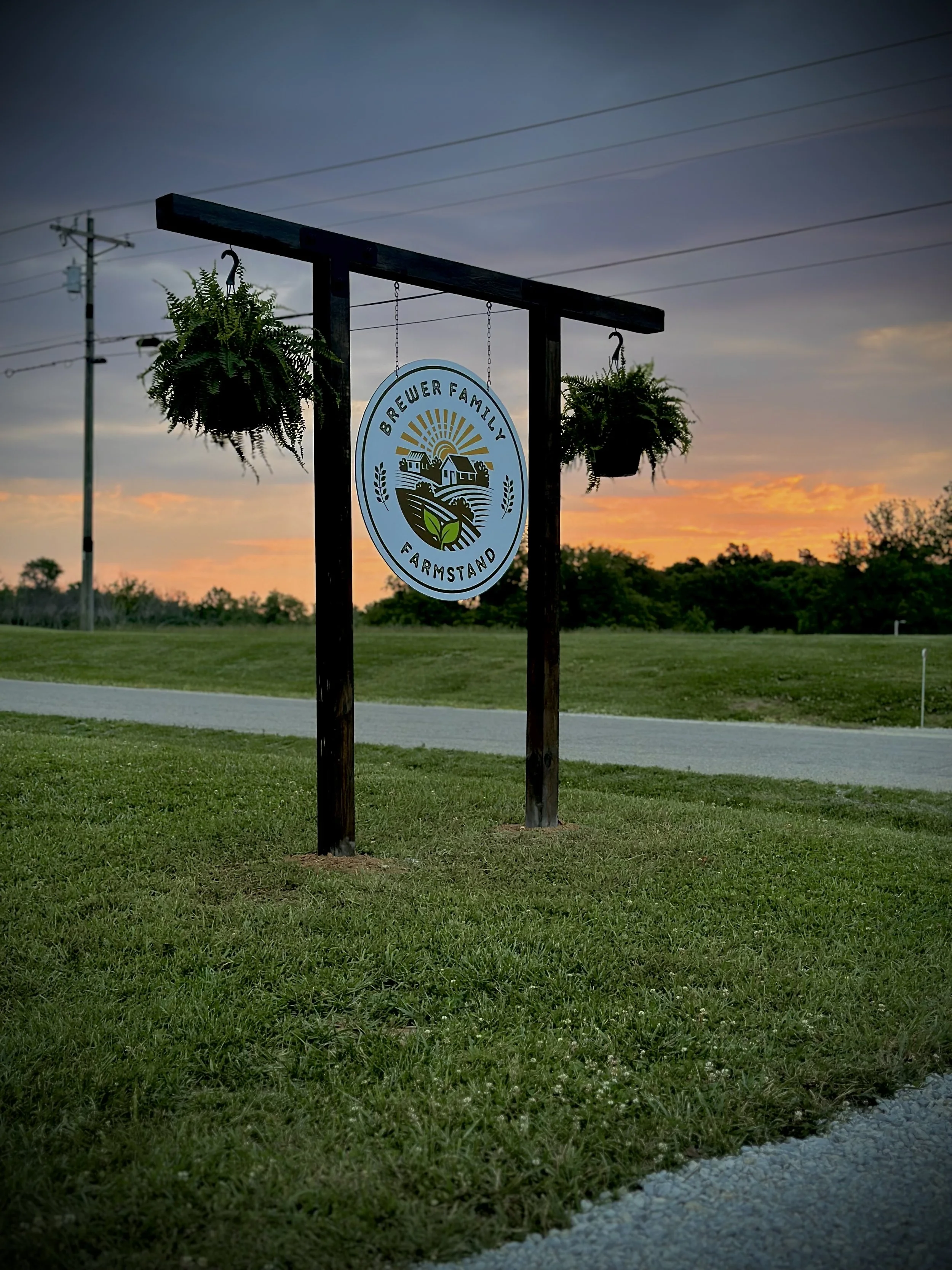 Wooden sign for Brewer Family Farmstand displayed outdoors at sunset on a rural homestead property.