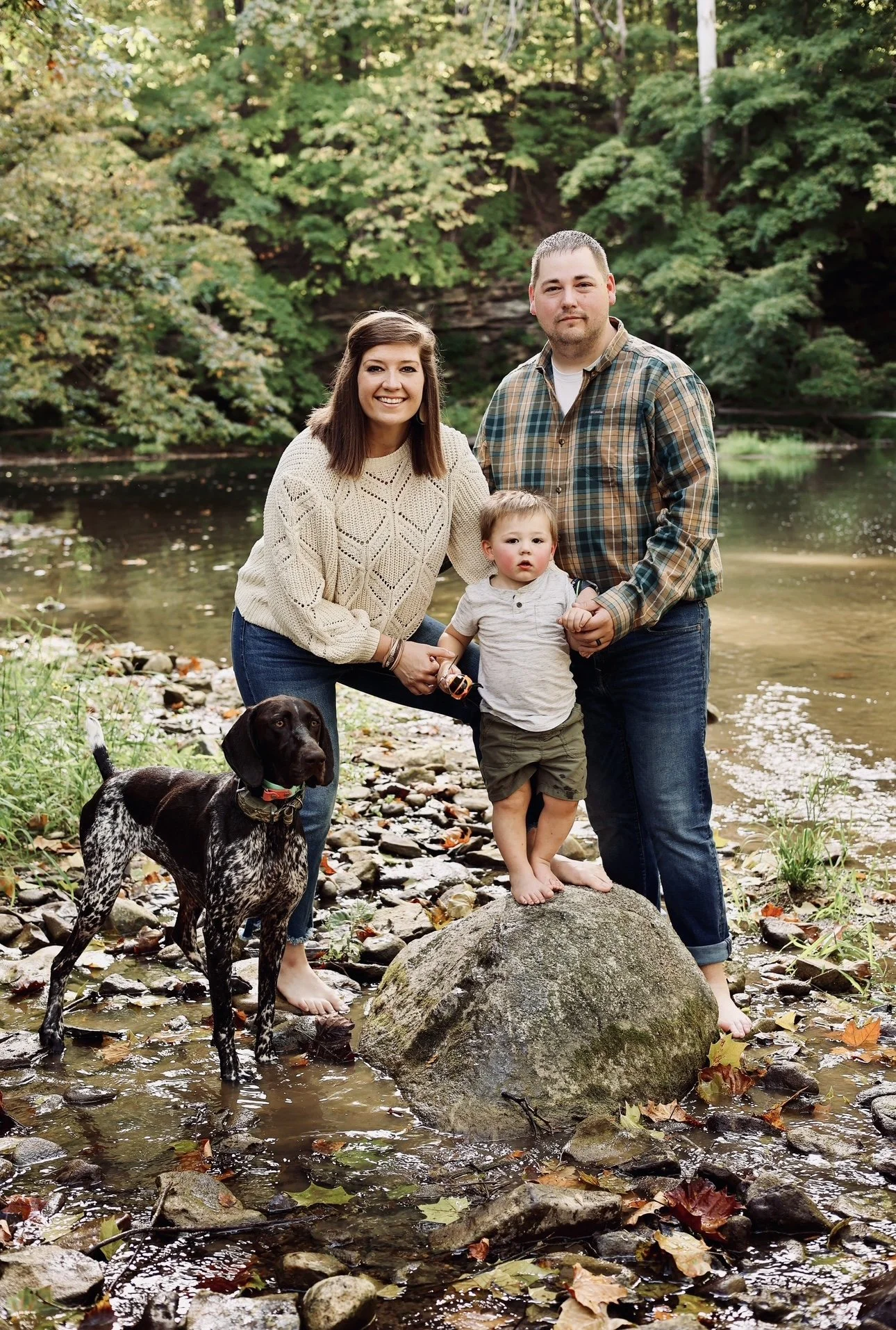 The Brewer family standing together along Coal Creek with their young son and family dog on their Indiana homestead.