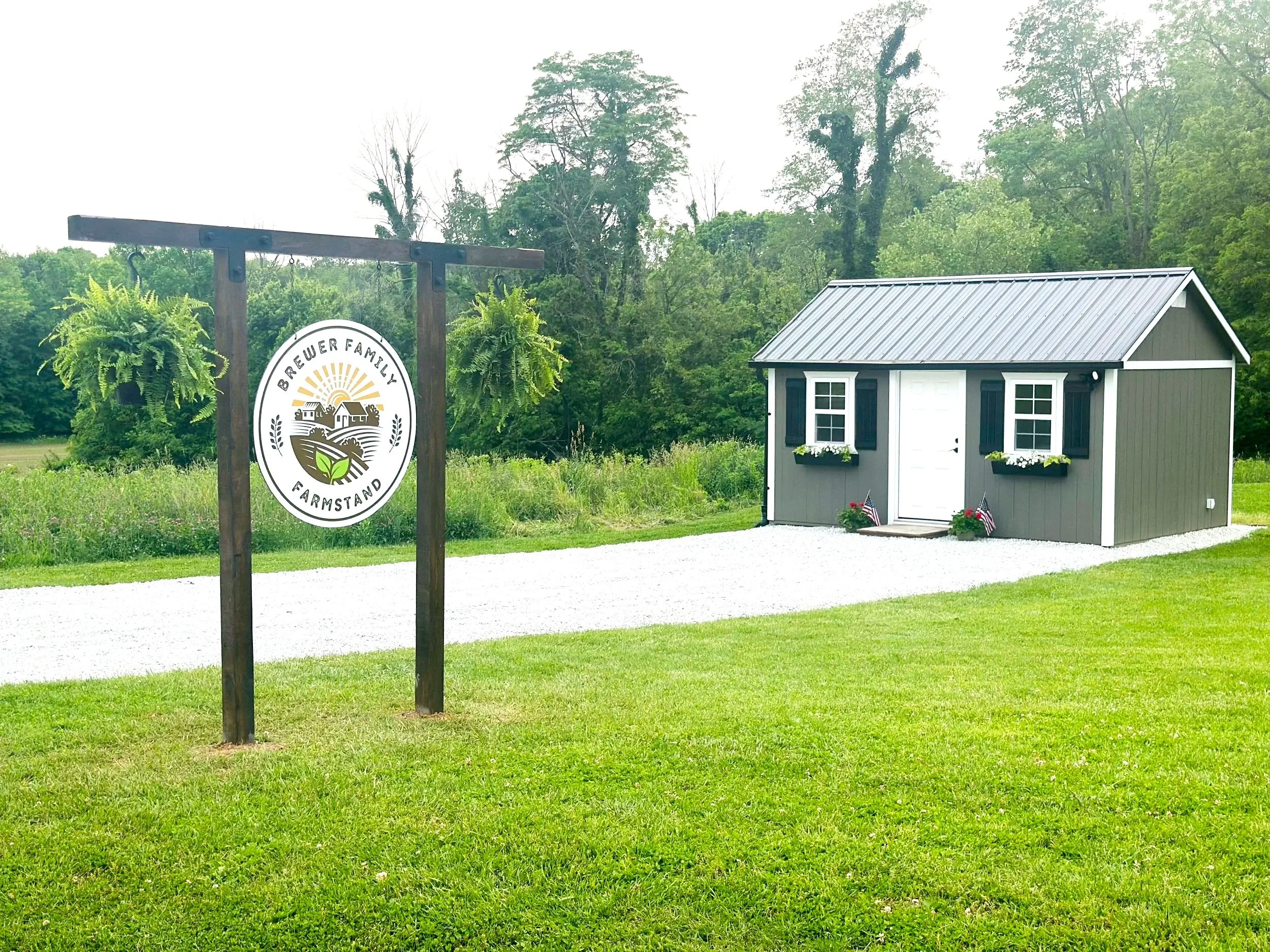 Brewer Family Farmstand self-serve farmstand building with roadside sign, gravel drive, and green pasture along Coal Creek in rural Indiana.