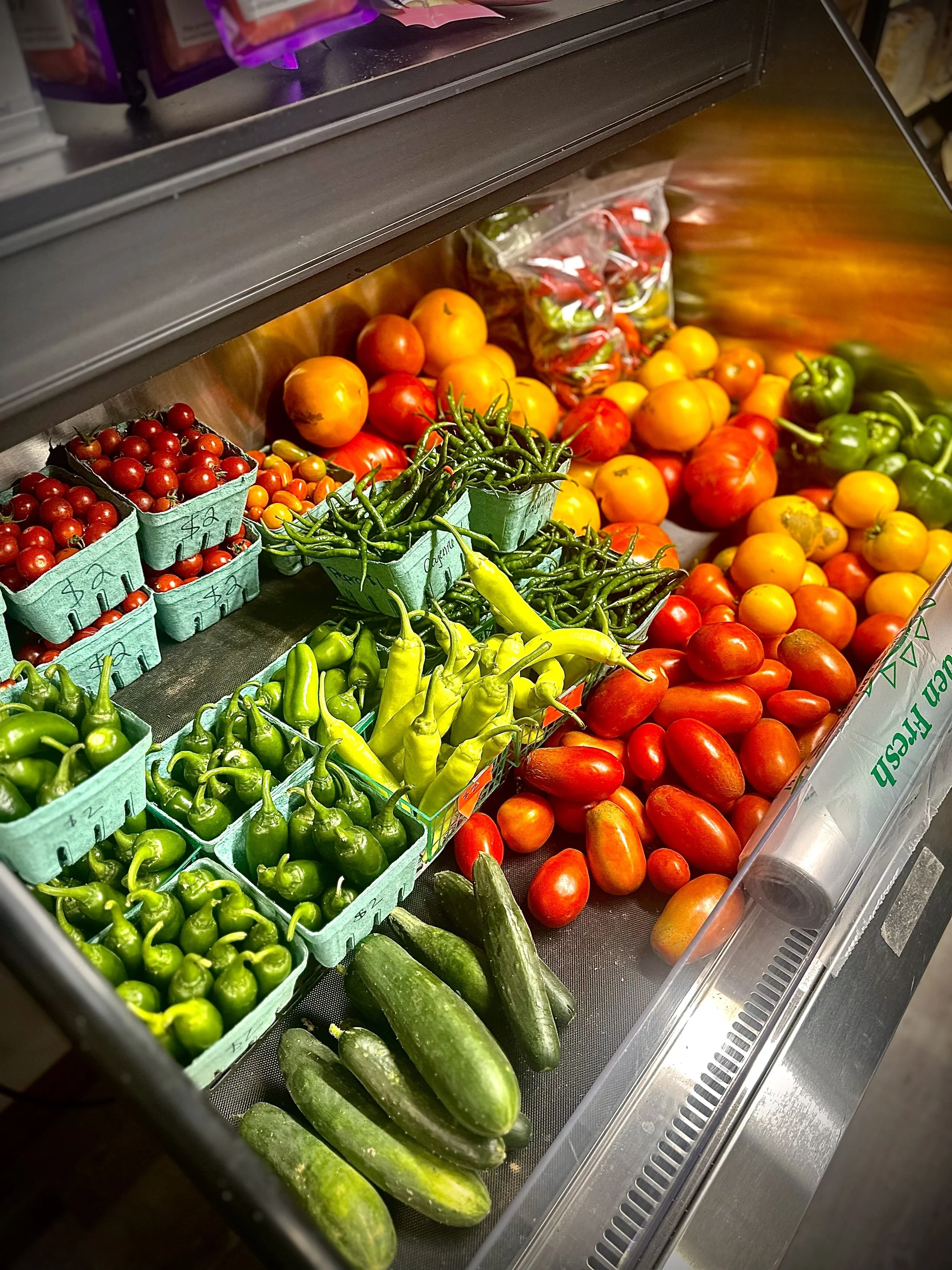 Display of fresh homegrown vegetables including tomatoes and green produce inside the Farmstand.