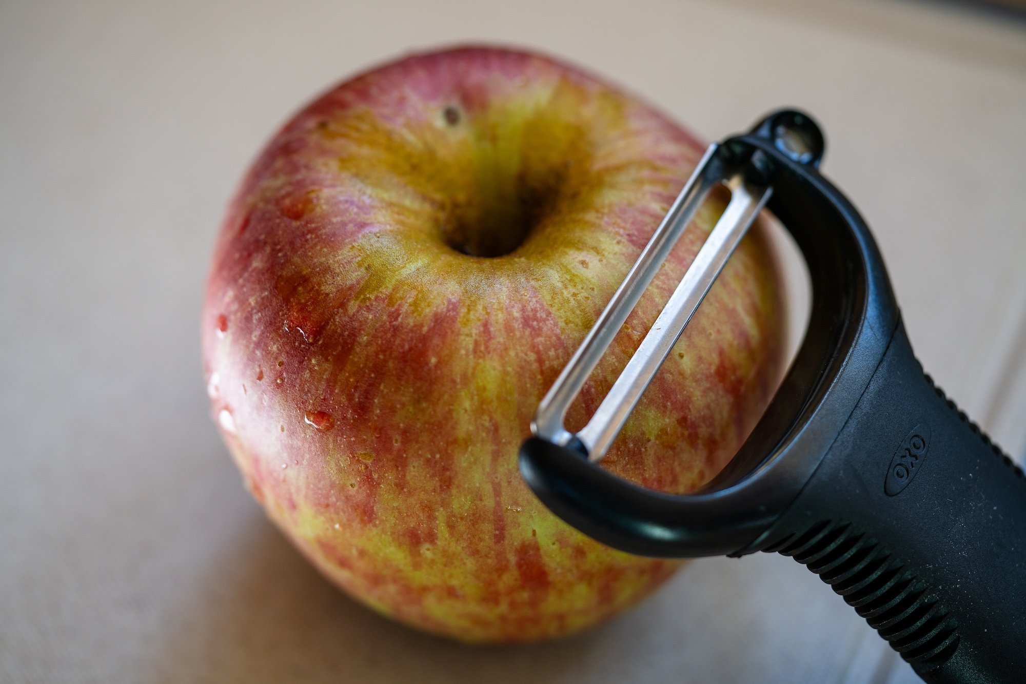 A fresh apple resting on a cutting board with an OXO Y-peeler beside it, ready to be peeled for baking.
