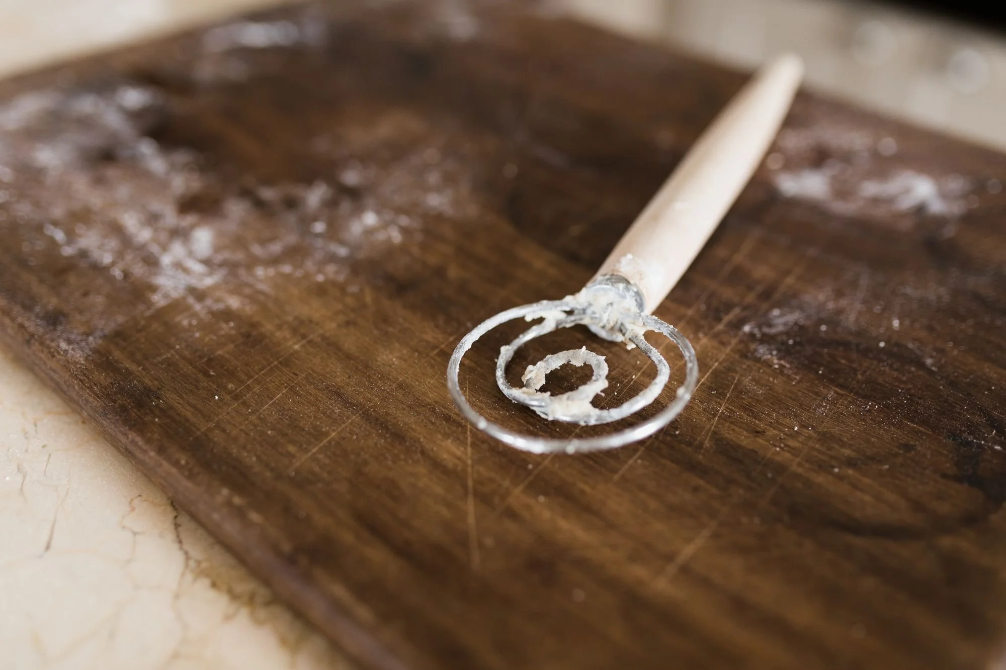 Close-up of a Danish whisk with dough residue on a wooden board, used to mix sourdough dough.