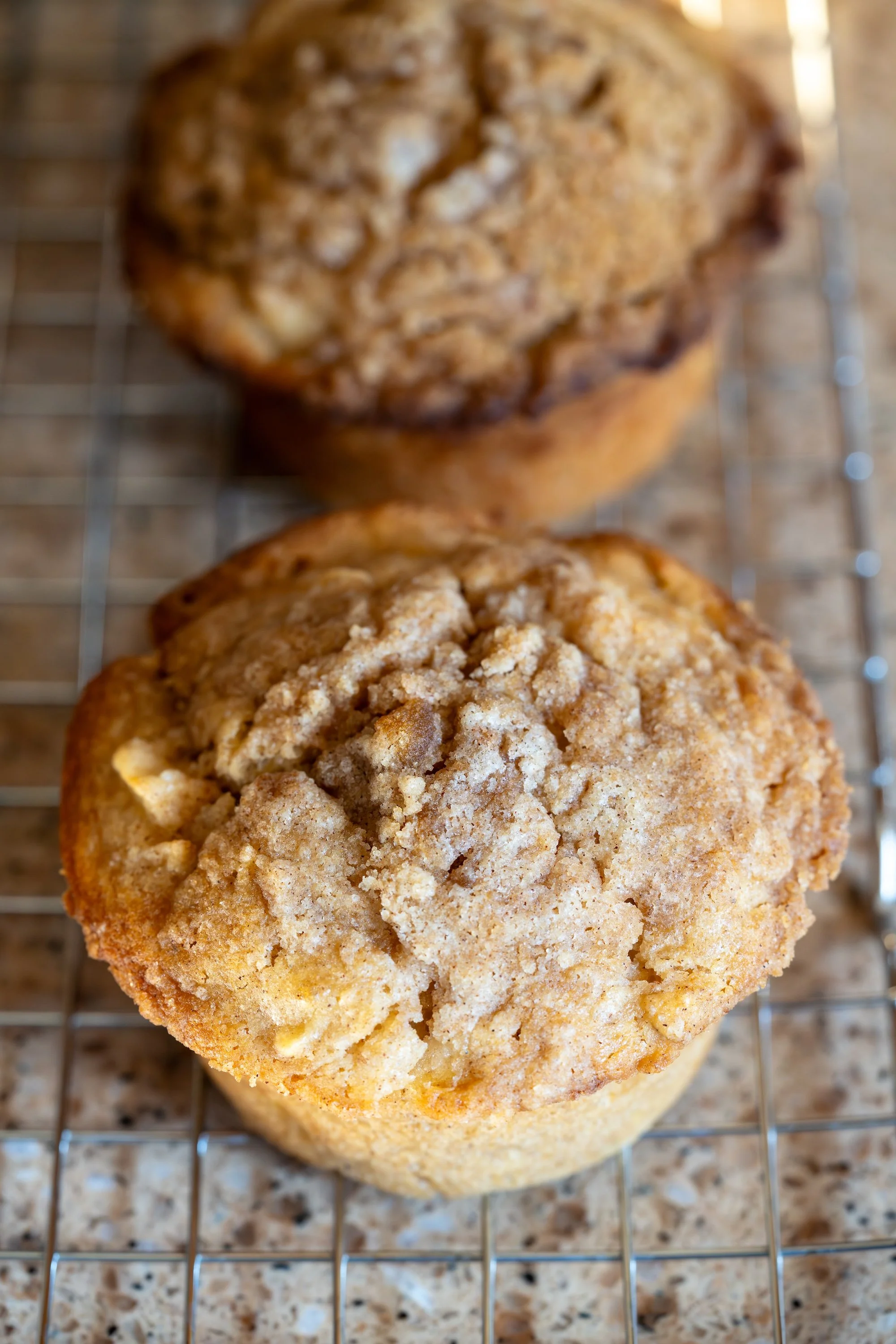 Two jumbo apple muffins cooling on a wire rack, topped with a golden cinnamon streusel.
