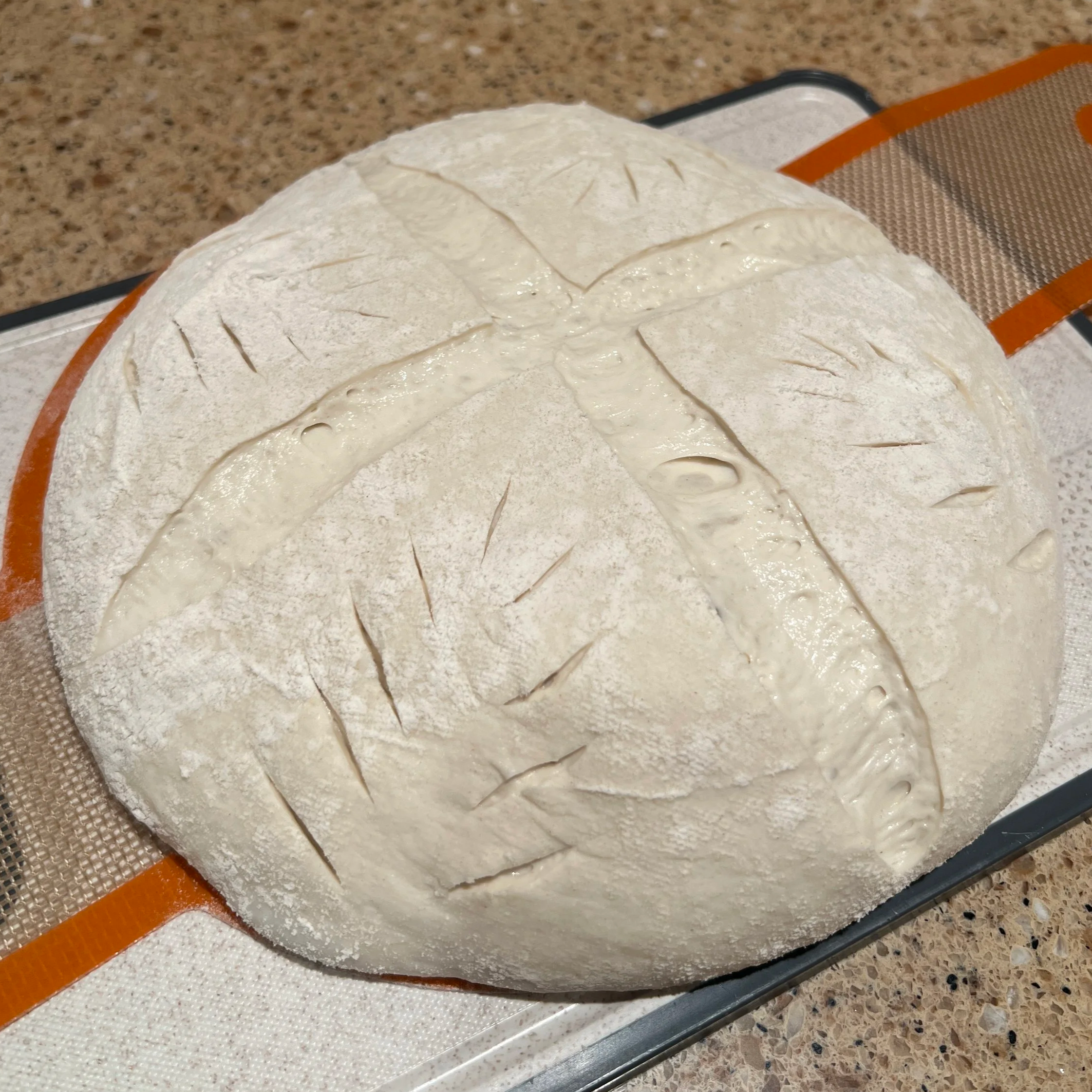 Cold-proofed sourdough loaf dusted with flour and scored with a cross pattern, resting on a silicone baking mat before baking.