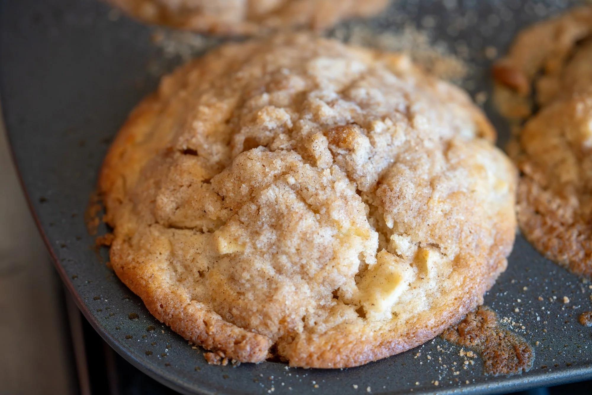 Freshly baked apple-cinnamon muffin with a cracked, golden streusel top still in the muffin pan.