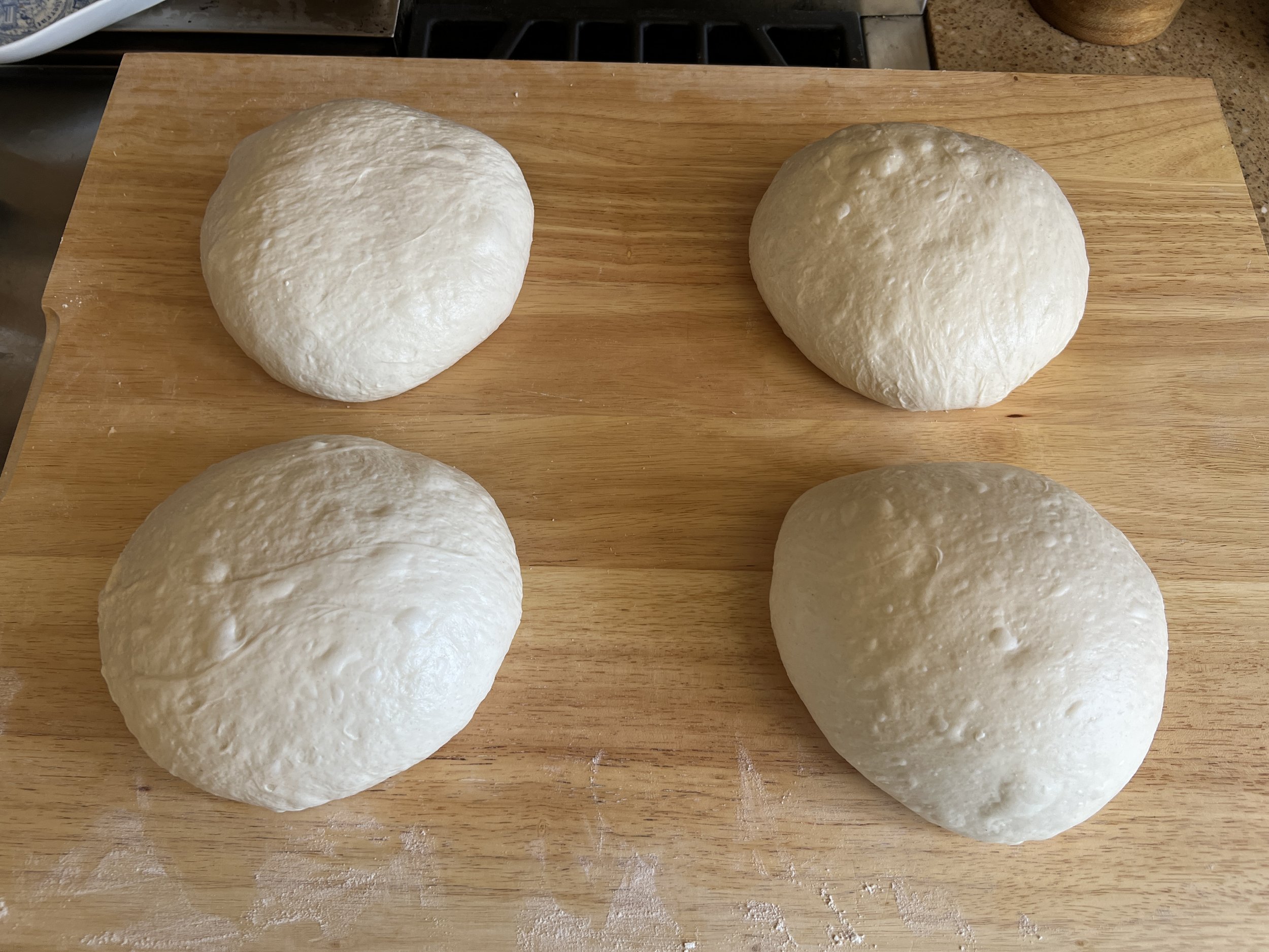 Four portions of sourdough dough preshaped into rounds, resting on a wooden cutting board during bench rest.