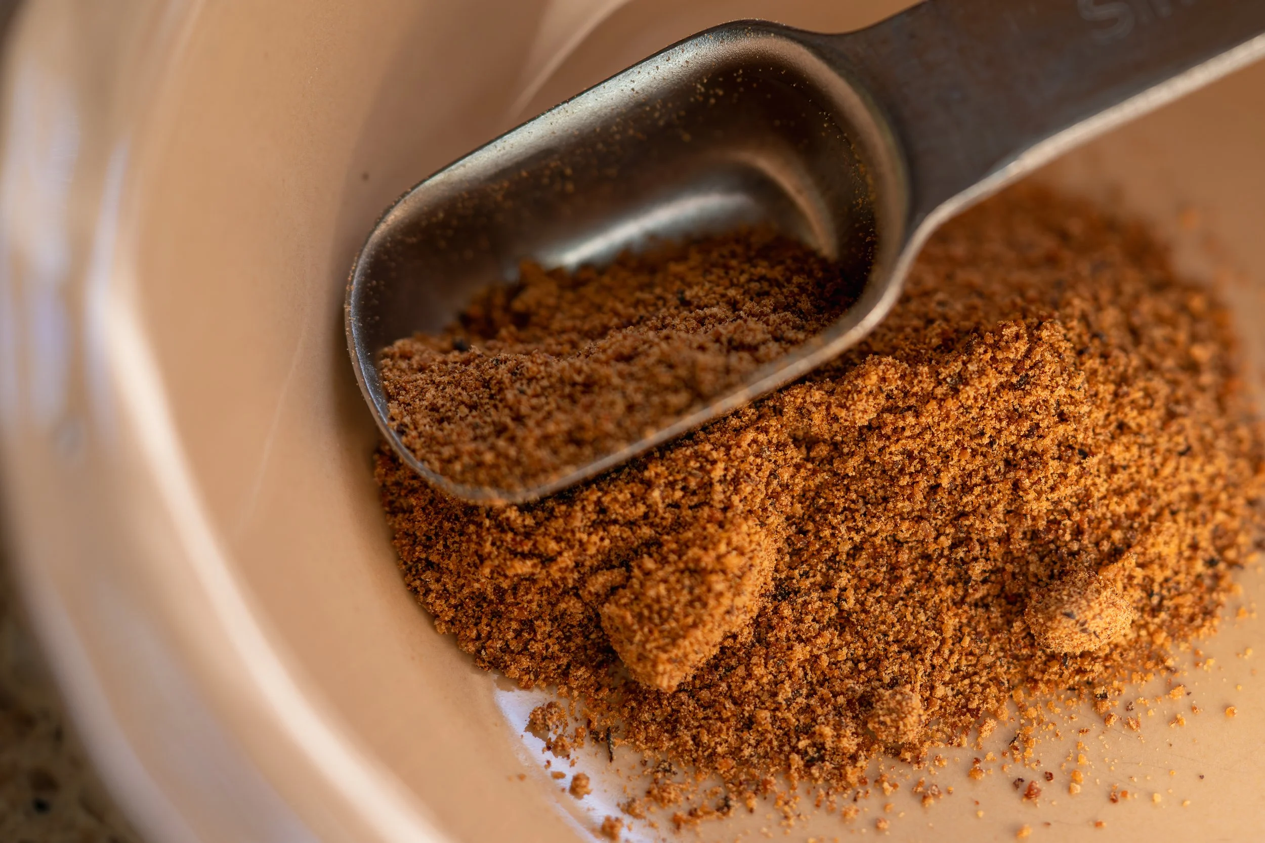 Close-up of ground nutmeg in a measuring scoop, showing its fine texture and warm brown color.