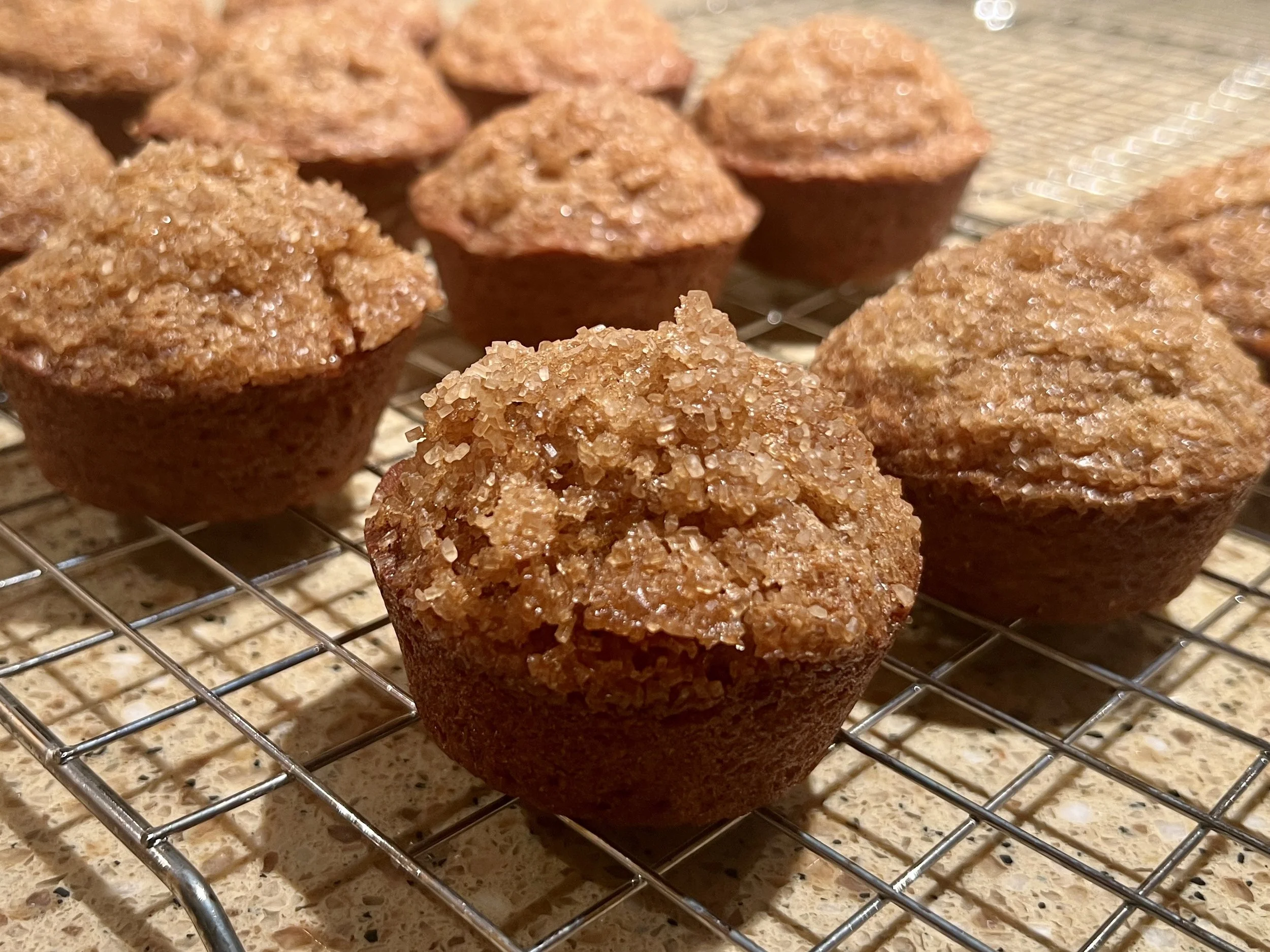 Close-up of banana muffins cooling on a wire rack, with coarse turbinado sugar on top giving them a crisp, golden texture.