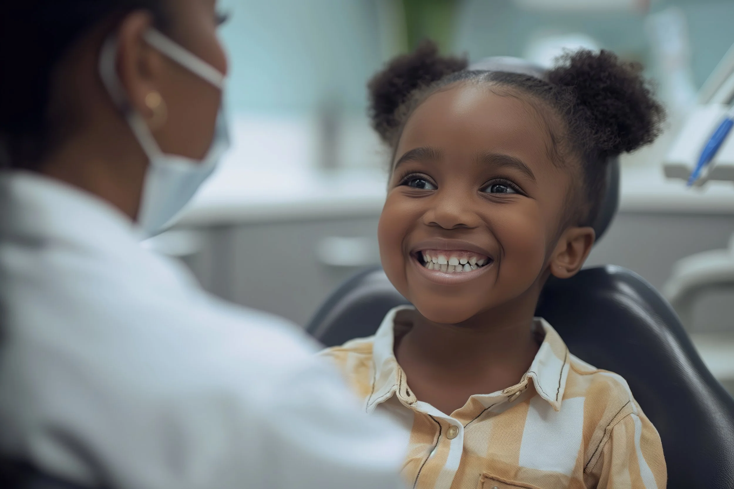 A young girl with puffy hair sitting in a dental chair, smiling happily while talking to a dentist wearing a mask. Chicago Dental Anesthesia sedation Illinois