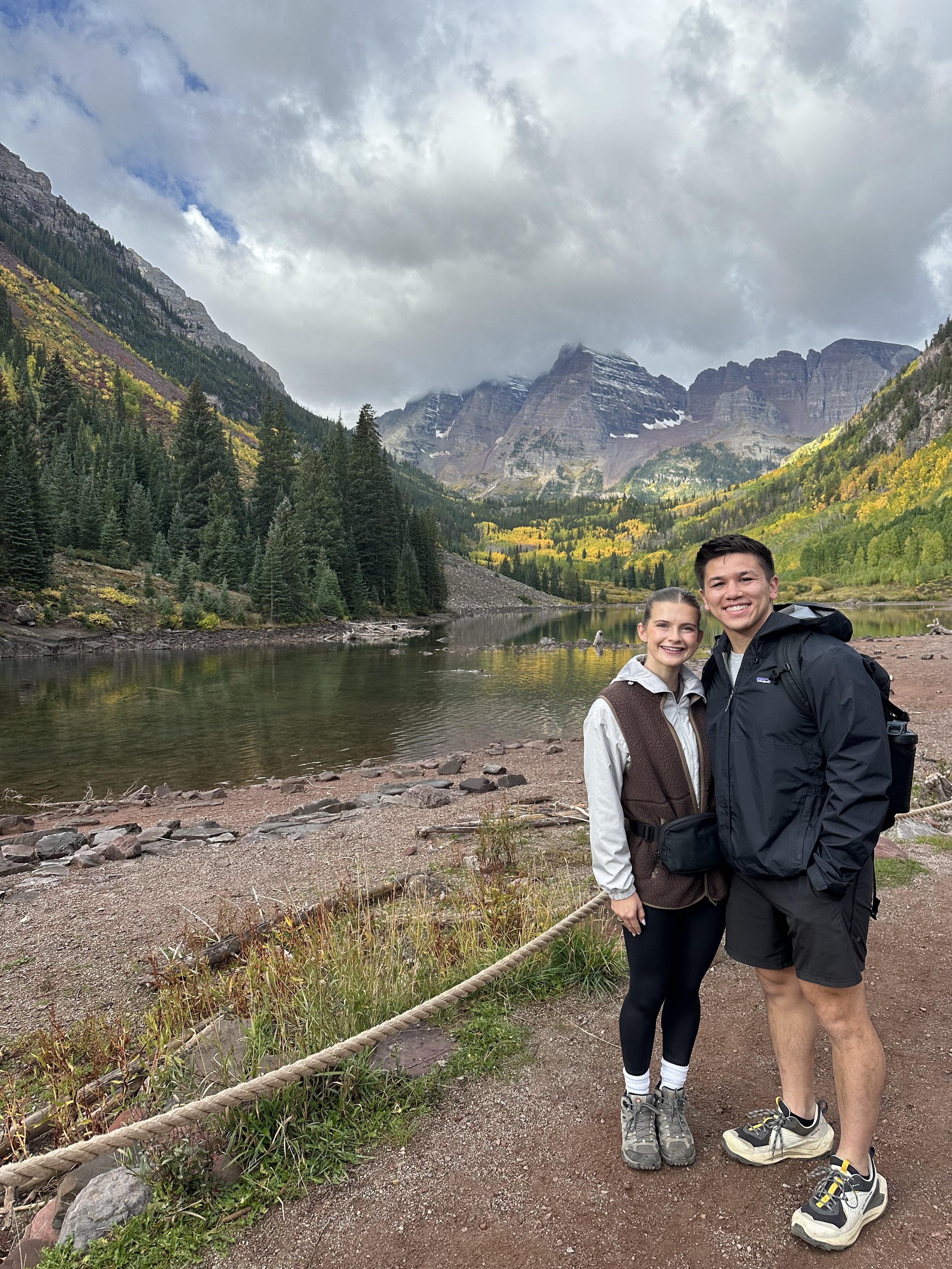 A young couple stands together outdoors during daytime with a mountain lake, forested mountains, and cloudy sky in the background. Chicago Dental Anesthesia sedation Illinois