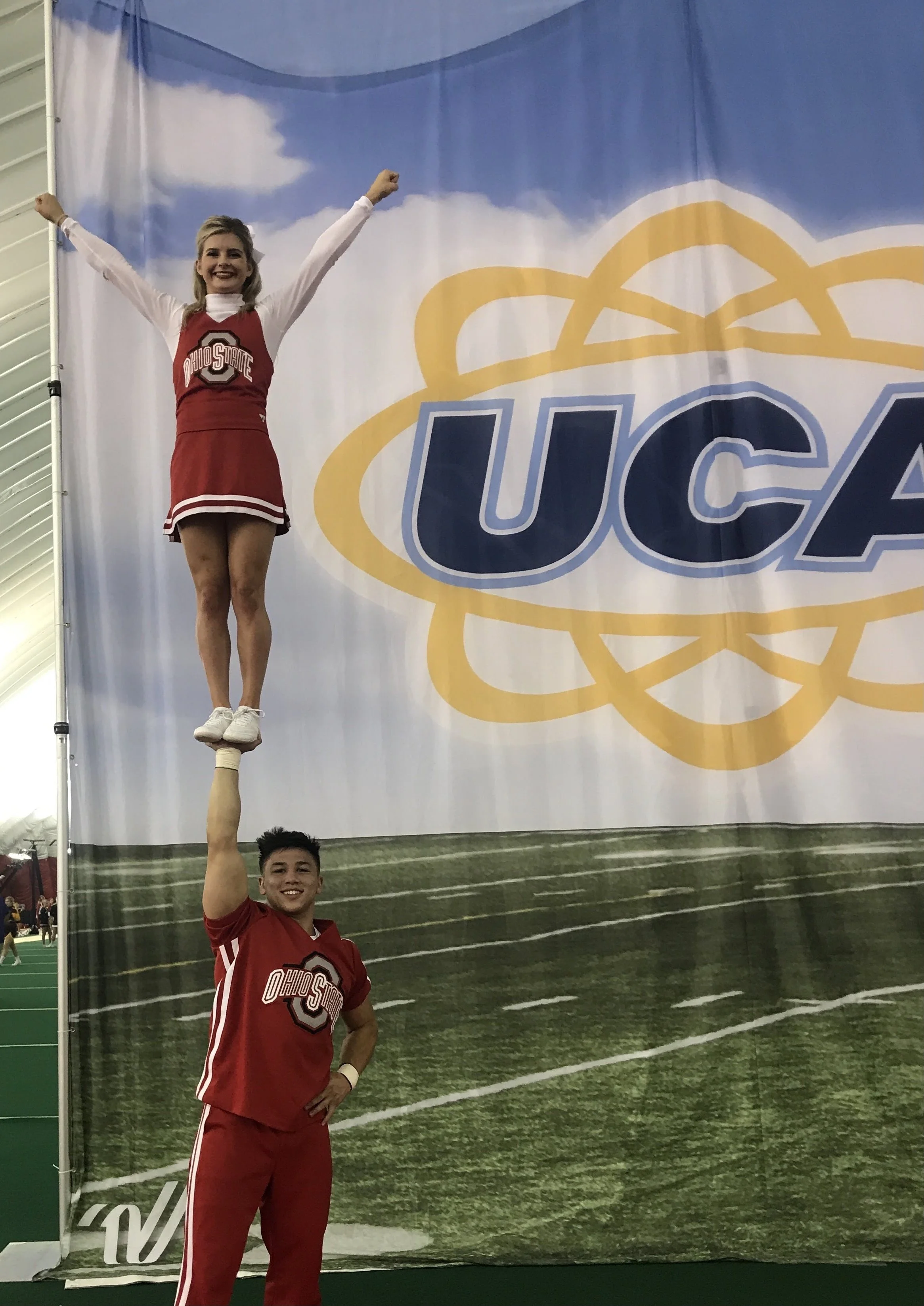 Cheerleader balancing on a male cheerleader's hand during an event with a UCA banner in the background. Chicago Dental Anesthesia sedation Illinois