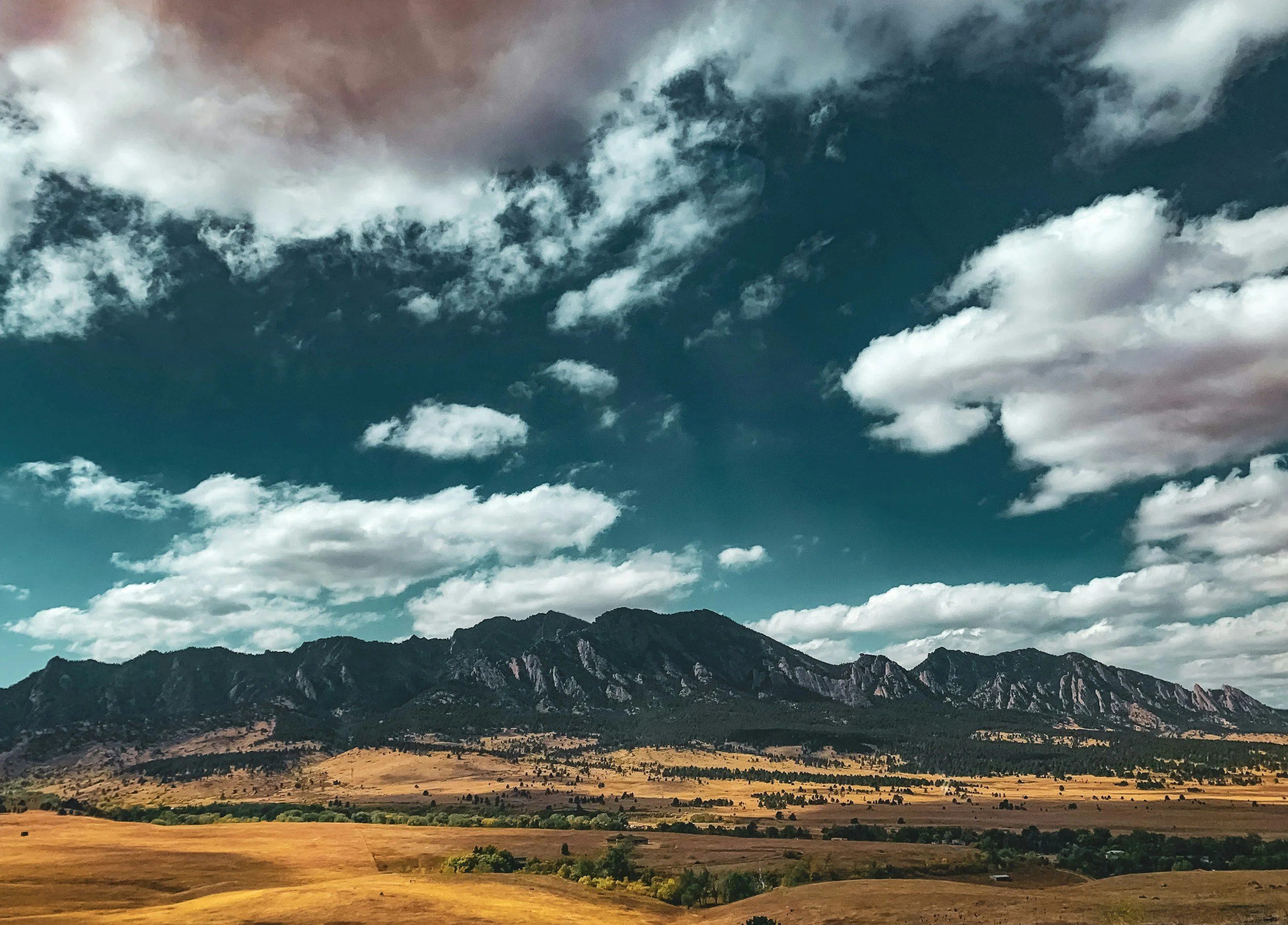 Landscape featuring a mountain range under a partly cloudy sky with a golden field in the foreground.