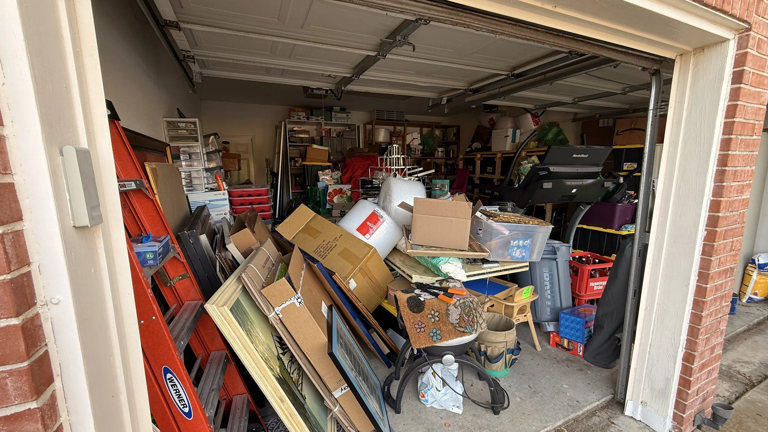 Cluttered garage with boxes, tools, and household items.