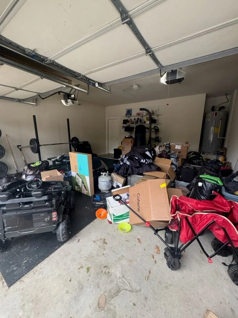 Garage with various toys, boxes, and equipment scattered around, including a red and black foldable wagon, a toy vehicle, and shelves with items in the background.