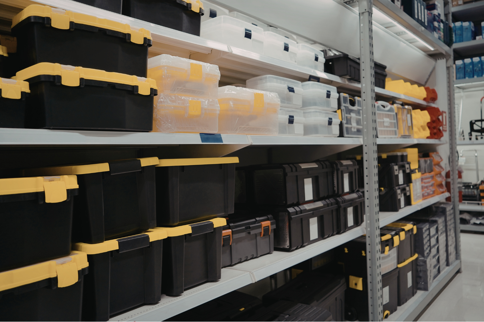 Store shelves filled with black, yellow, transparent, and orange plastic storage containers and toolboxes.