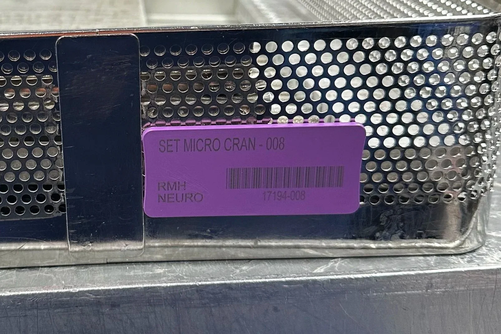 Close-up of a metal medical device with a purple label attached, which reads 'SET MICRO CRAN - 008', 'RMH NEURO', and has a barcode and serial number.